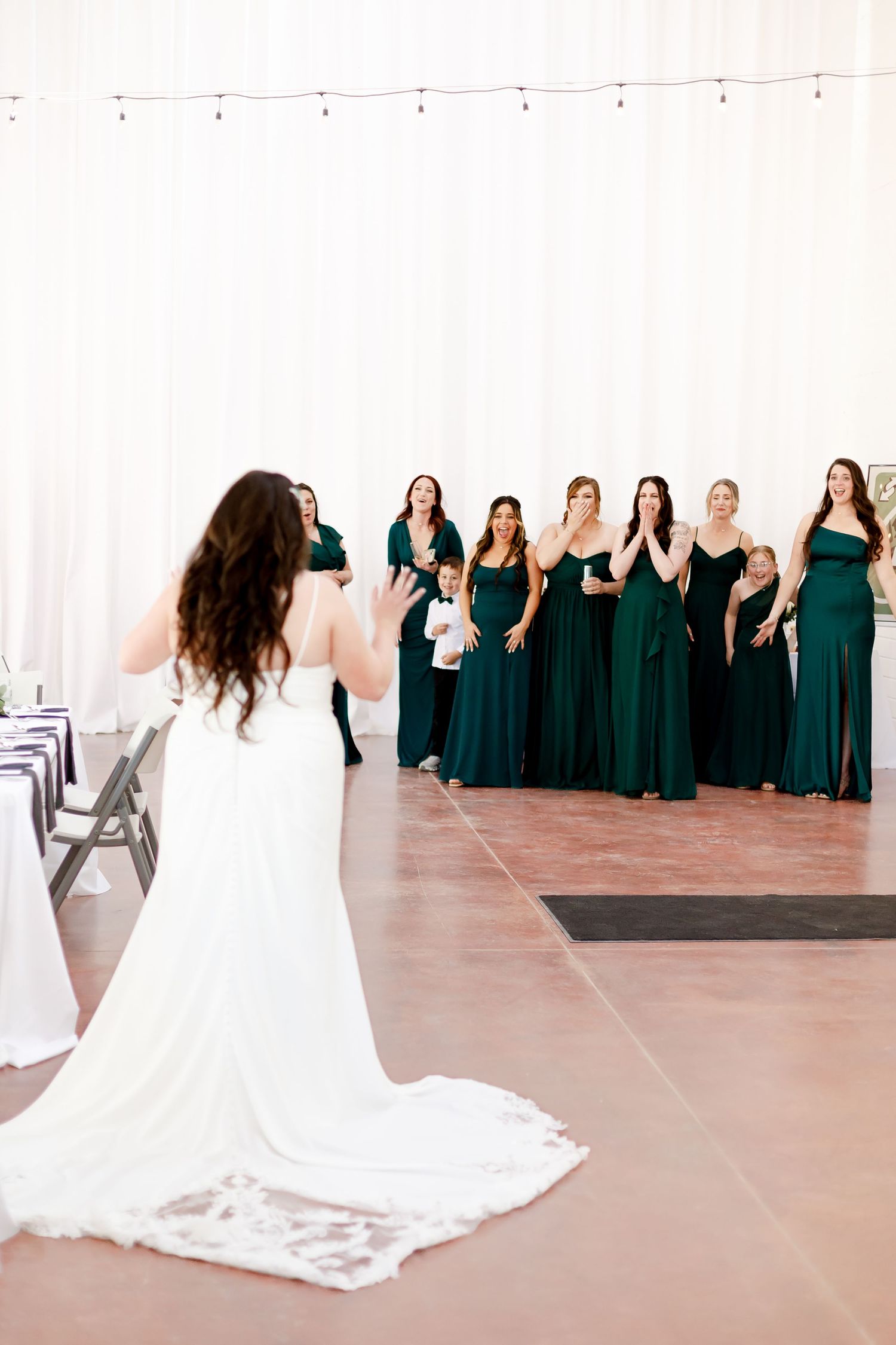 A photographer captures bridesmaids in matching emerald green dresses while the bride poses in a flowing white gown.