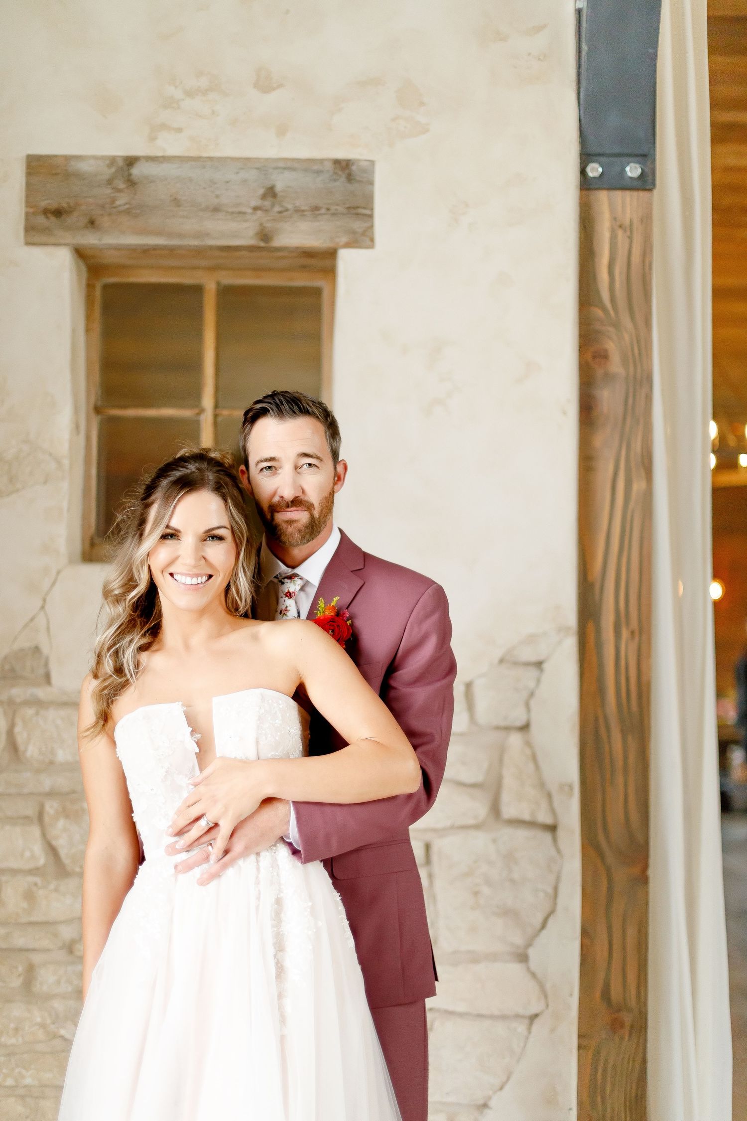 A happy wedding couple poses together against a rustic stone wall backdrop.