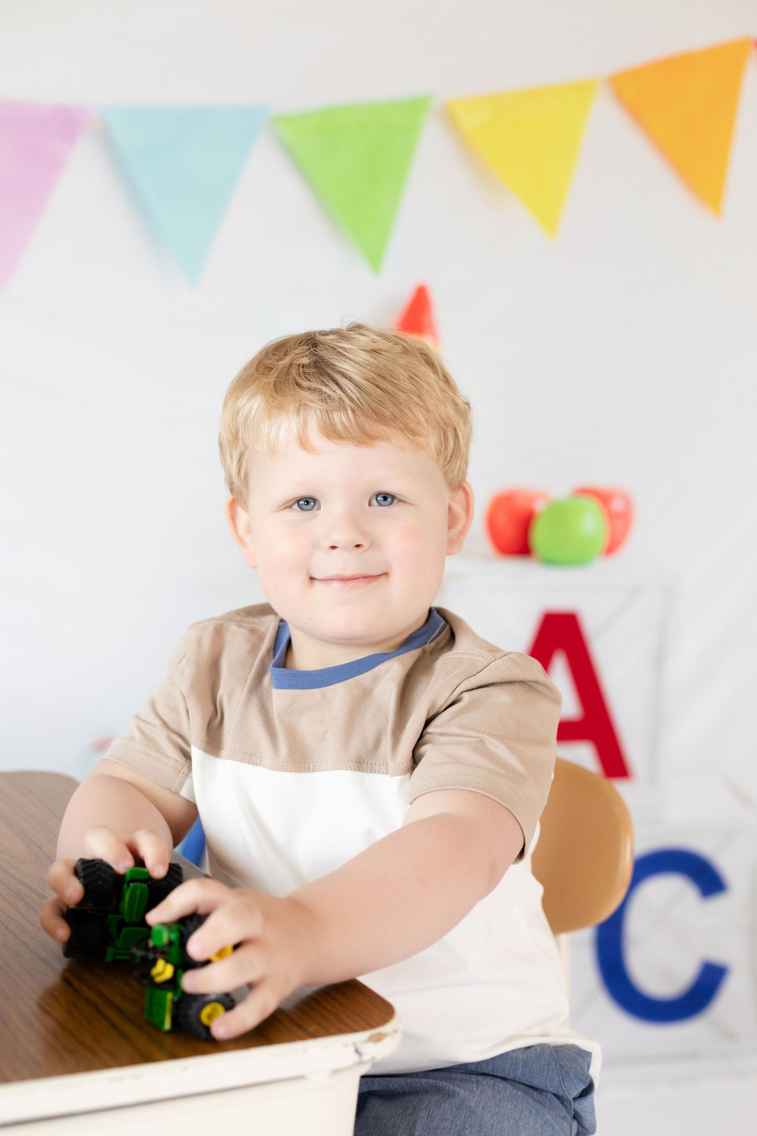 Child plays with toys at wooden table under festive bunting decorations in pastel colors.