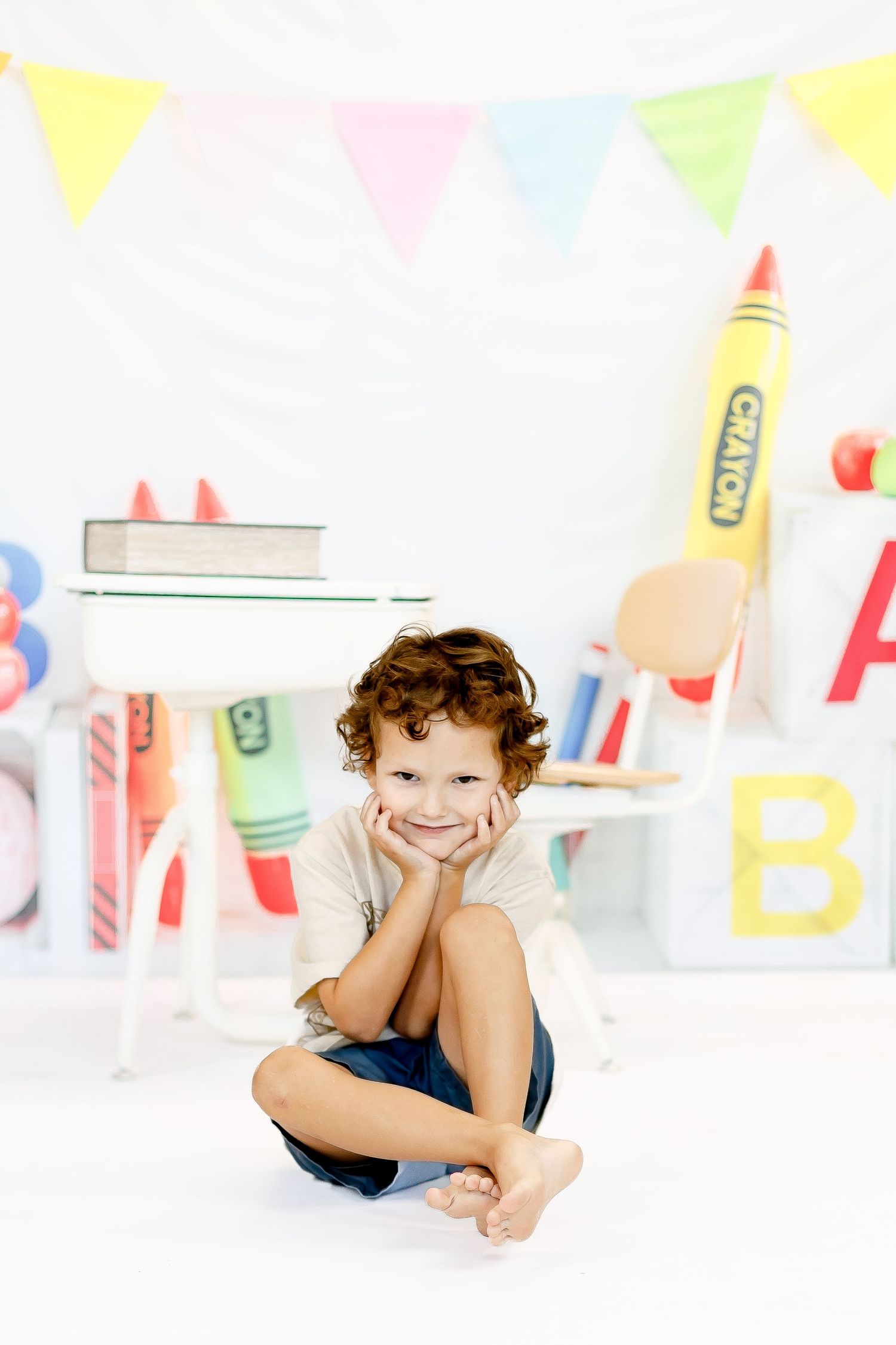 Young child lies on their stomach on white background with festive party flags and decorations overhead.