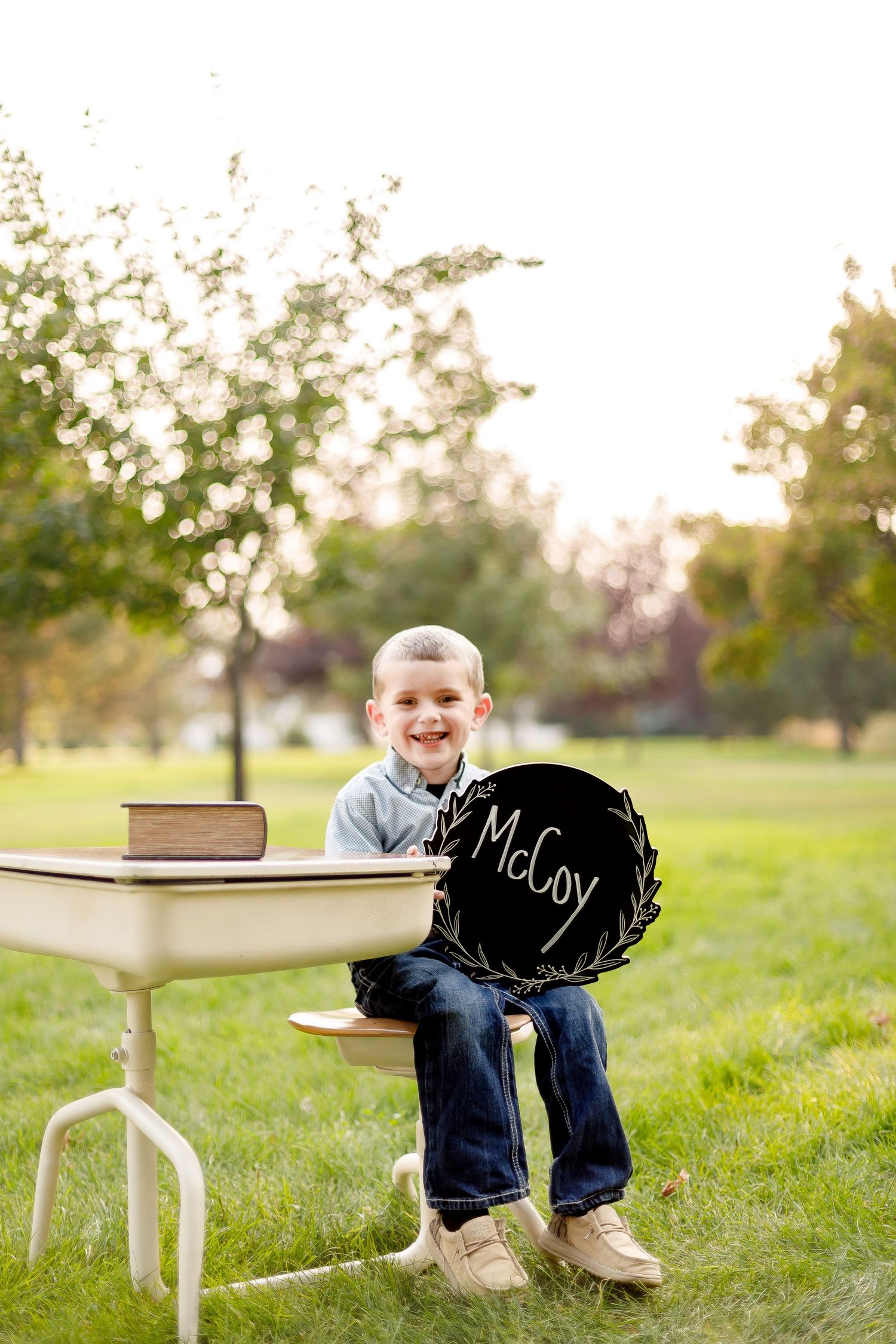 Three photos of a small child in jeans sitting at a white desk on grass at sunset.