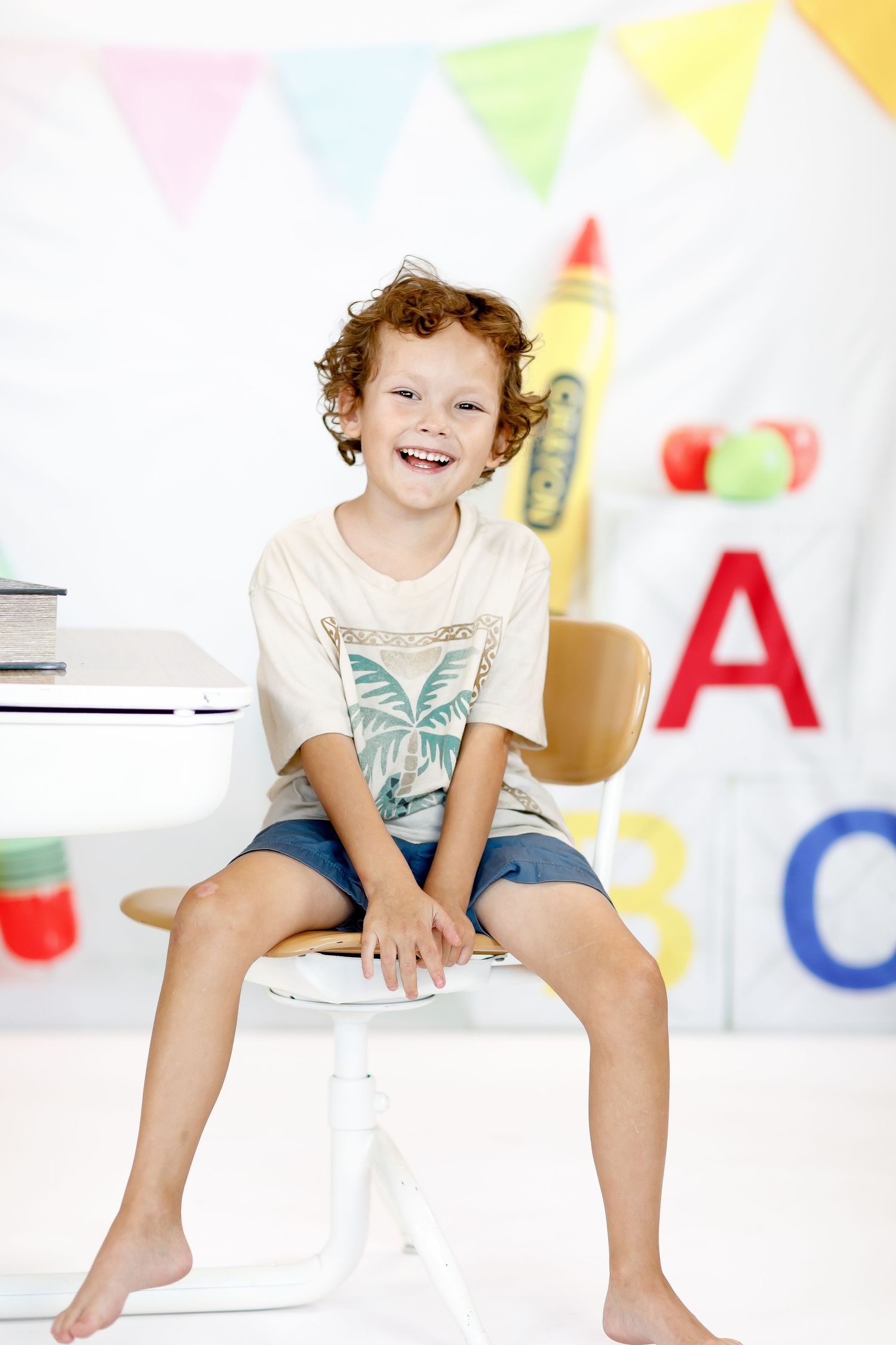 Cheerful child sitting in classroom decorated with colorful bunting and alphabet letters in background.