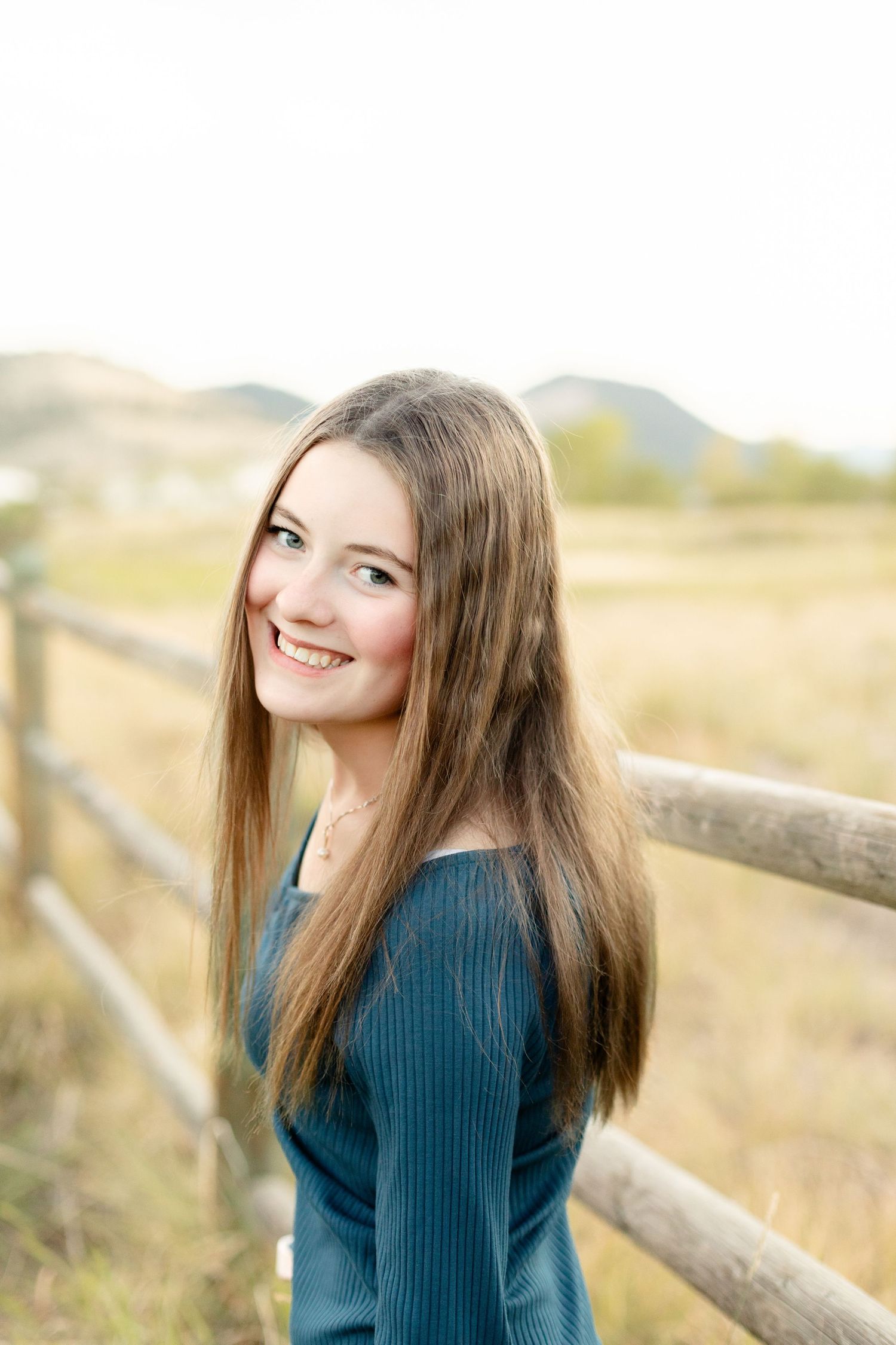 Casual outdoor portrait near rustic wooden fence with golden field in background.