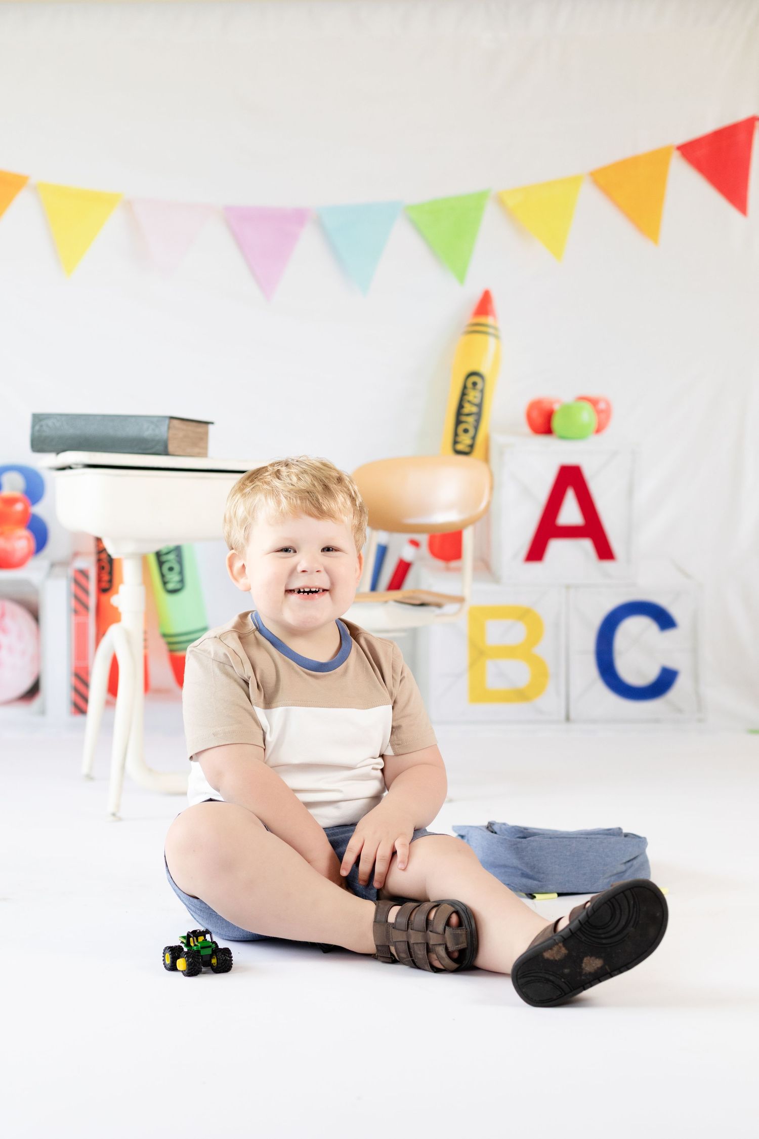 A young child sitting on studio floor with colorful birthday party decorations including ABC letters and pennant banners.