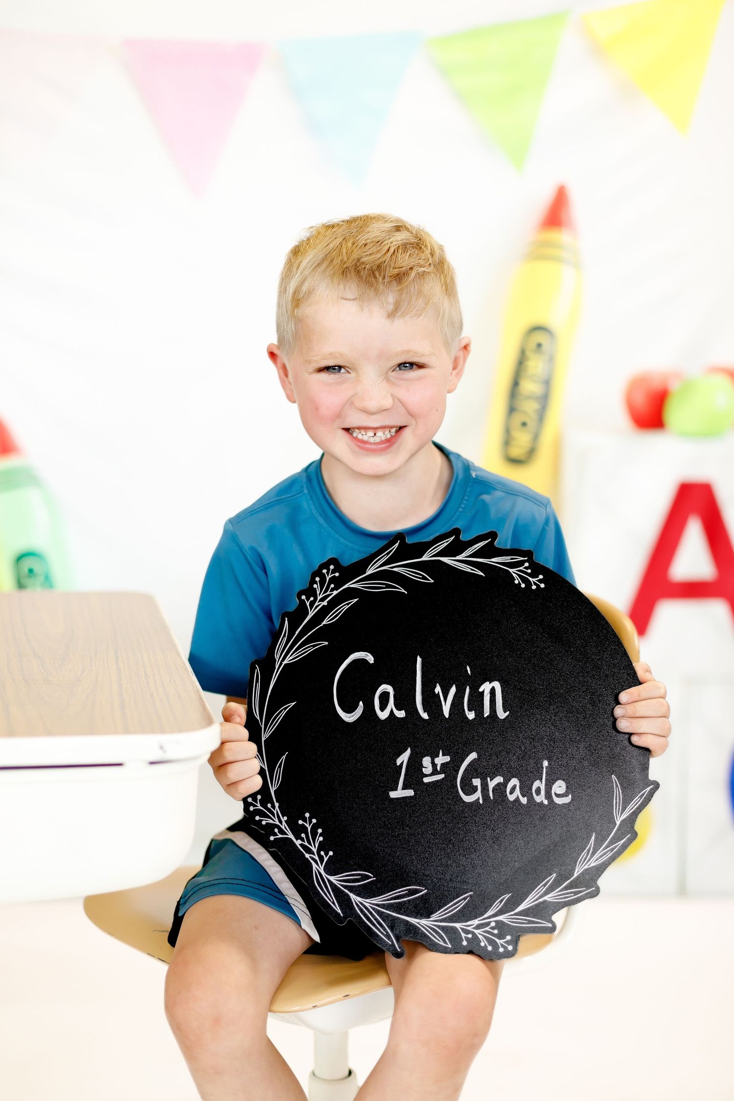 A child in a blue shirt holds up a decorative black chalkboard with handwritten text against a festive background.