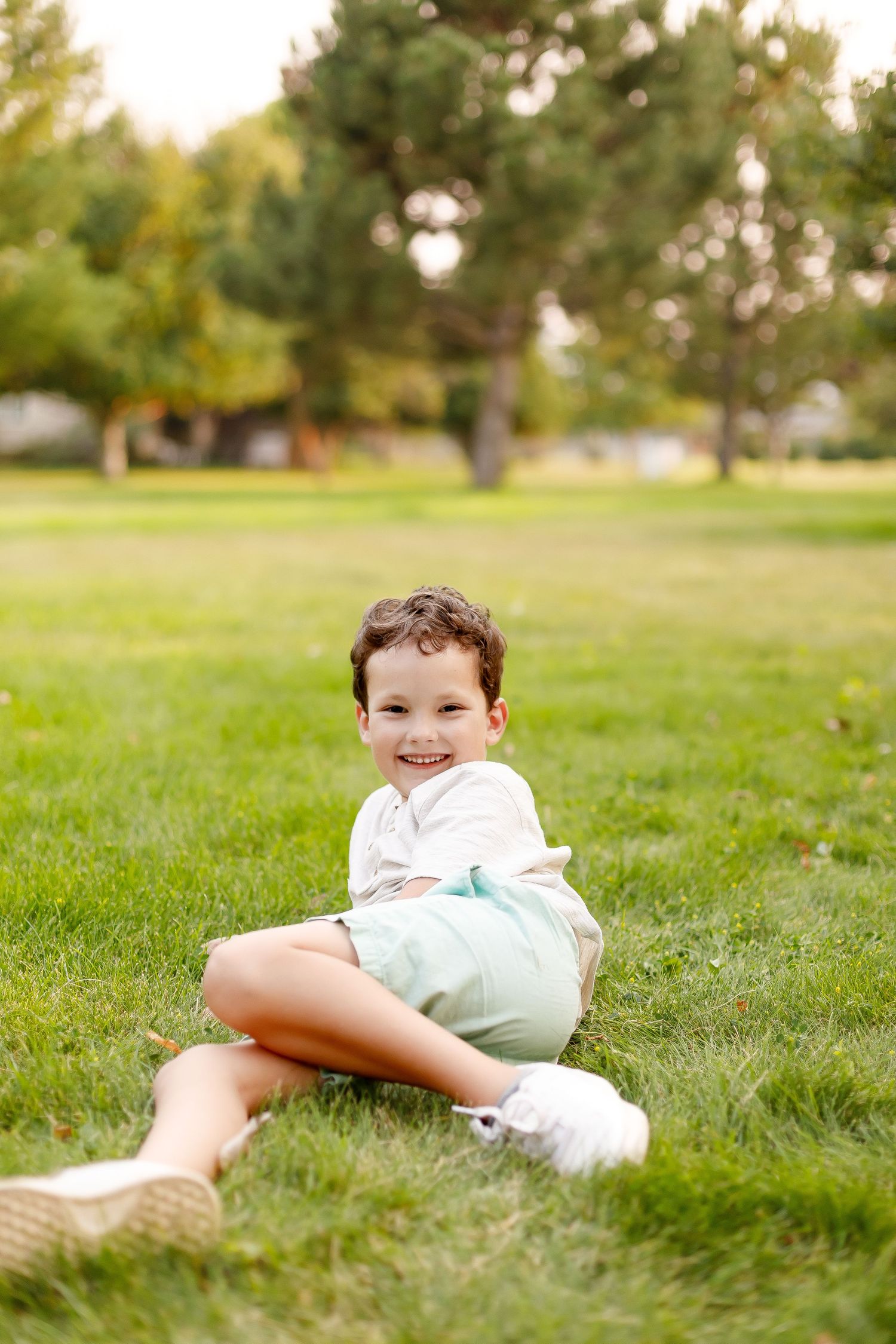 A person in a mint green outfit lies casually on lush grass in a sunny park setting.