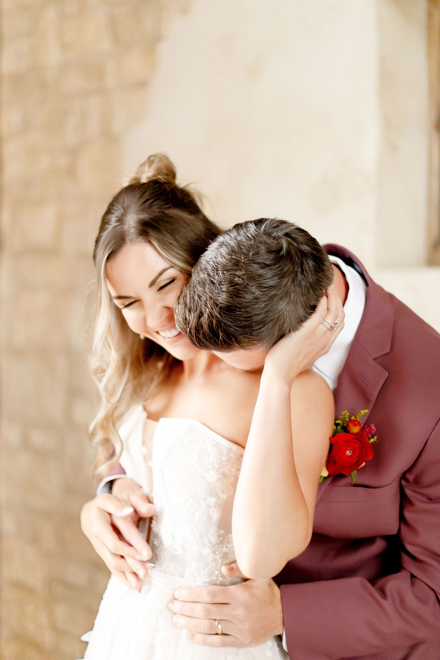 Couple in elegant wedding attire sharing an intimate moment against a stone wall background.