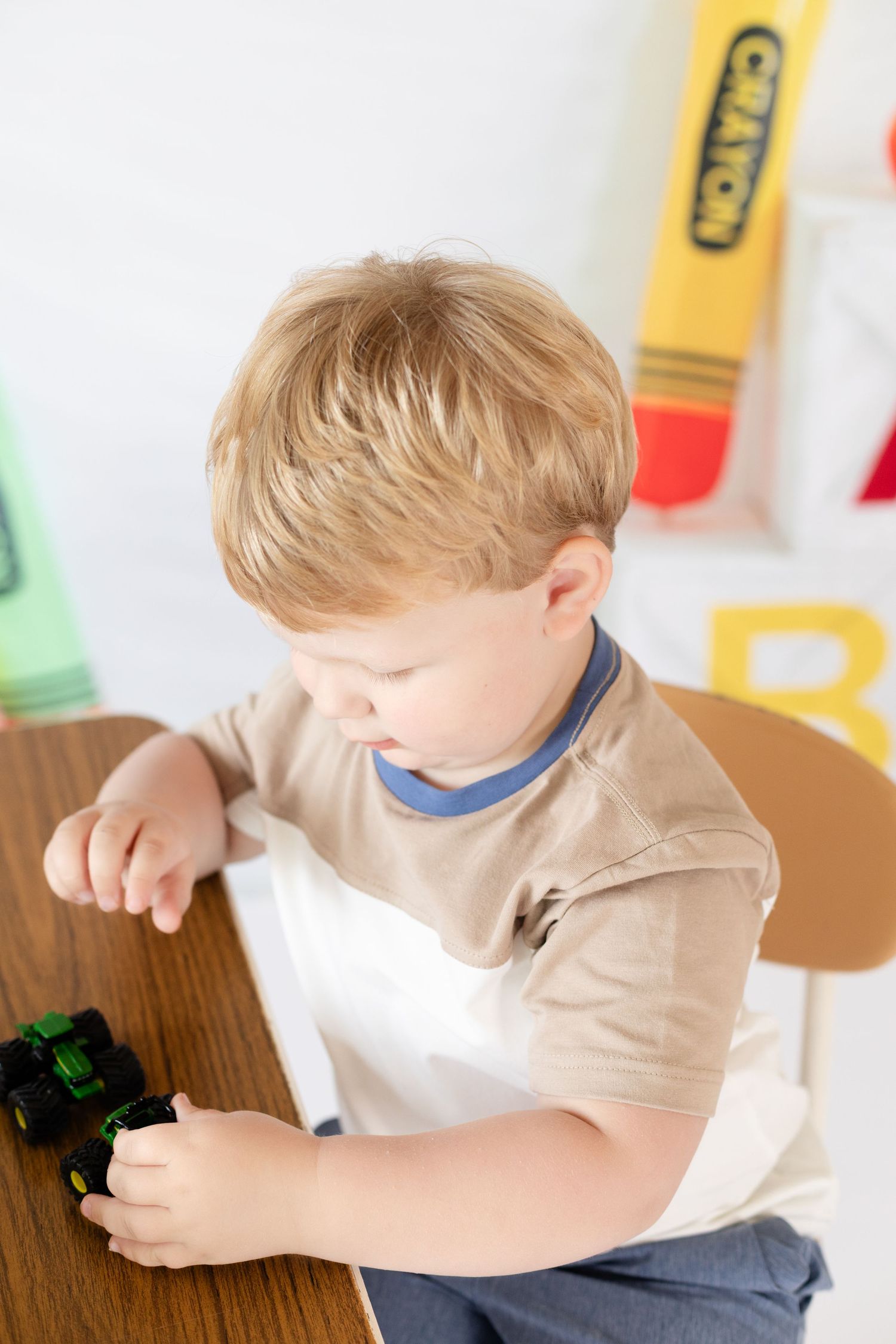 Child in tan shirt and blue collar plays with small toys on a wooden surface with a bright background.