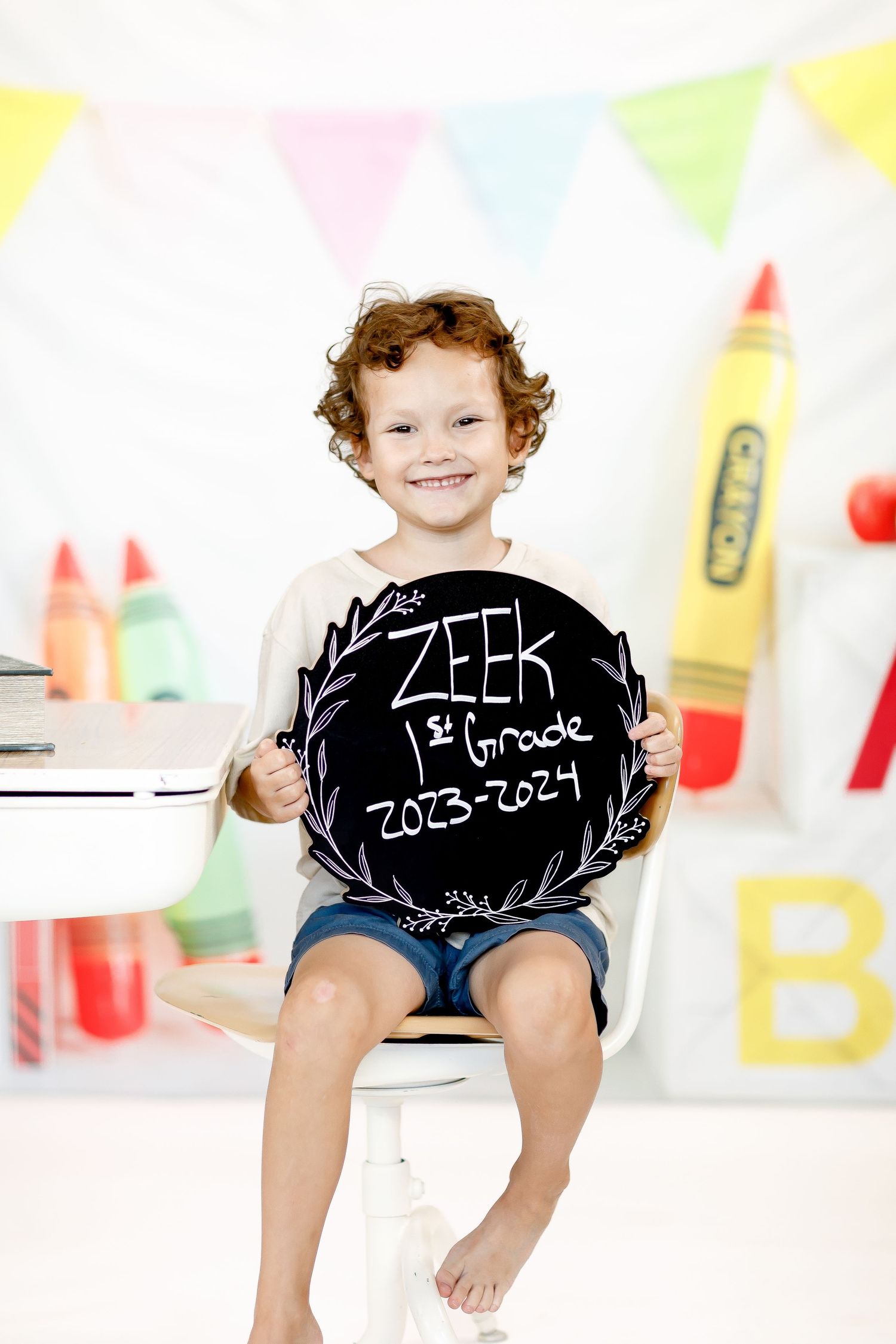 Toddler wearing black chalkboard shorts with dates written in chalk on a bright colored background.