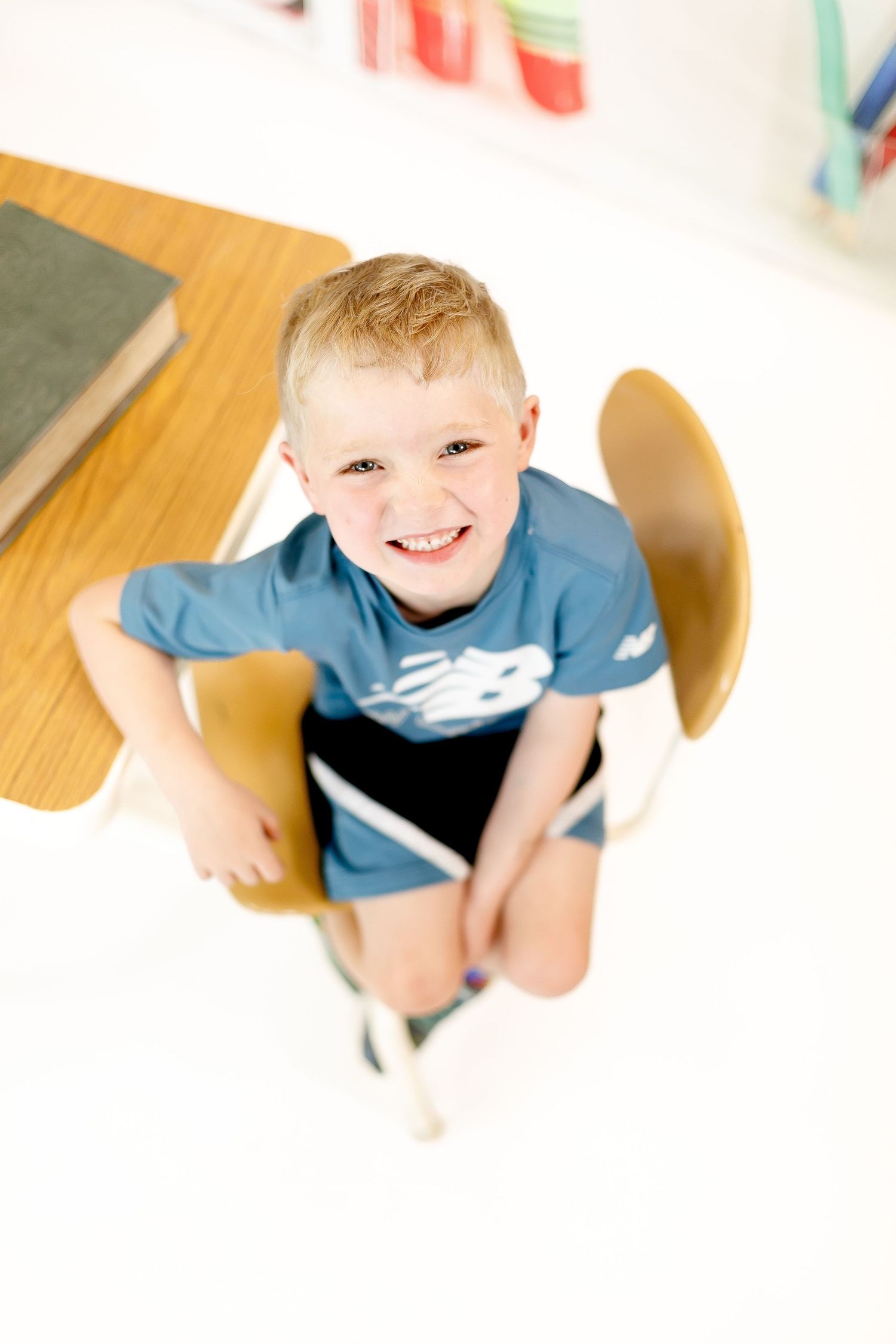 Child wearing a blue shirt seated at a wooden table explores learning materials with animated expressions.