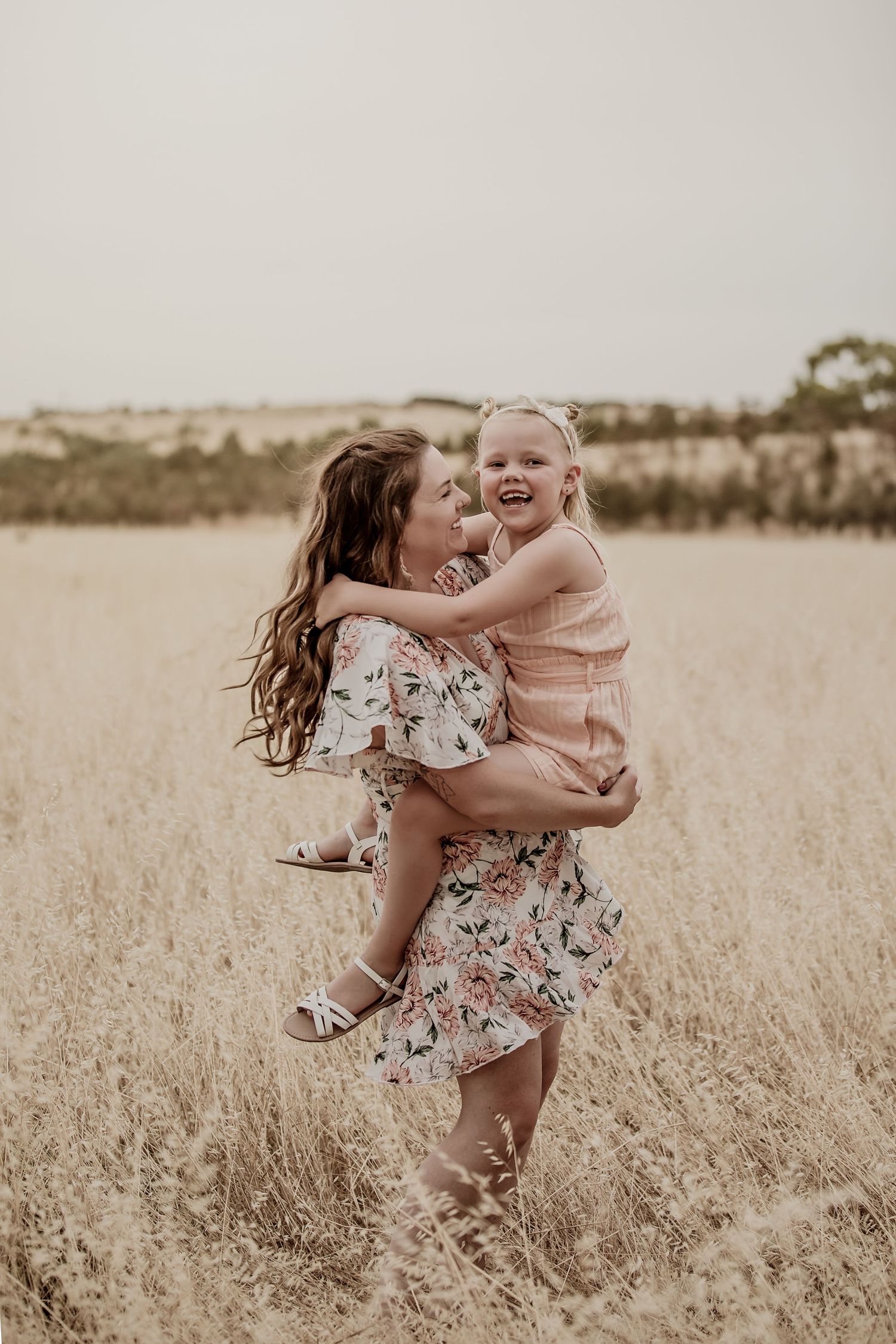 Chloe White the photographer smiling as she gives her daughter a piggy back in a field.