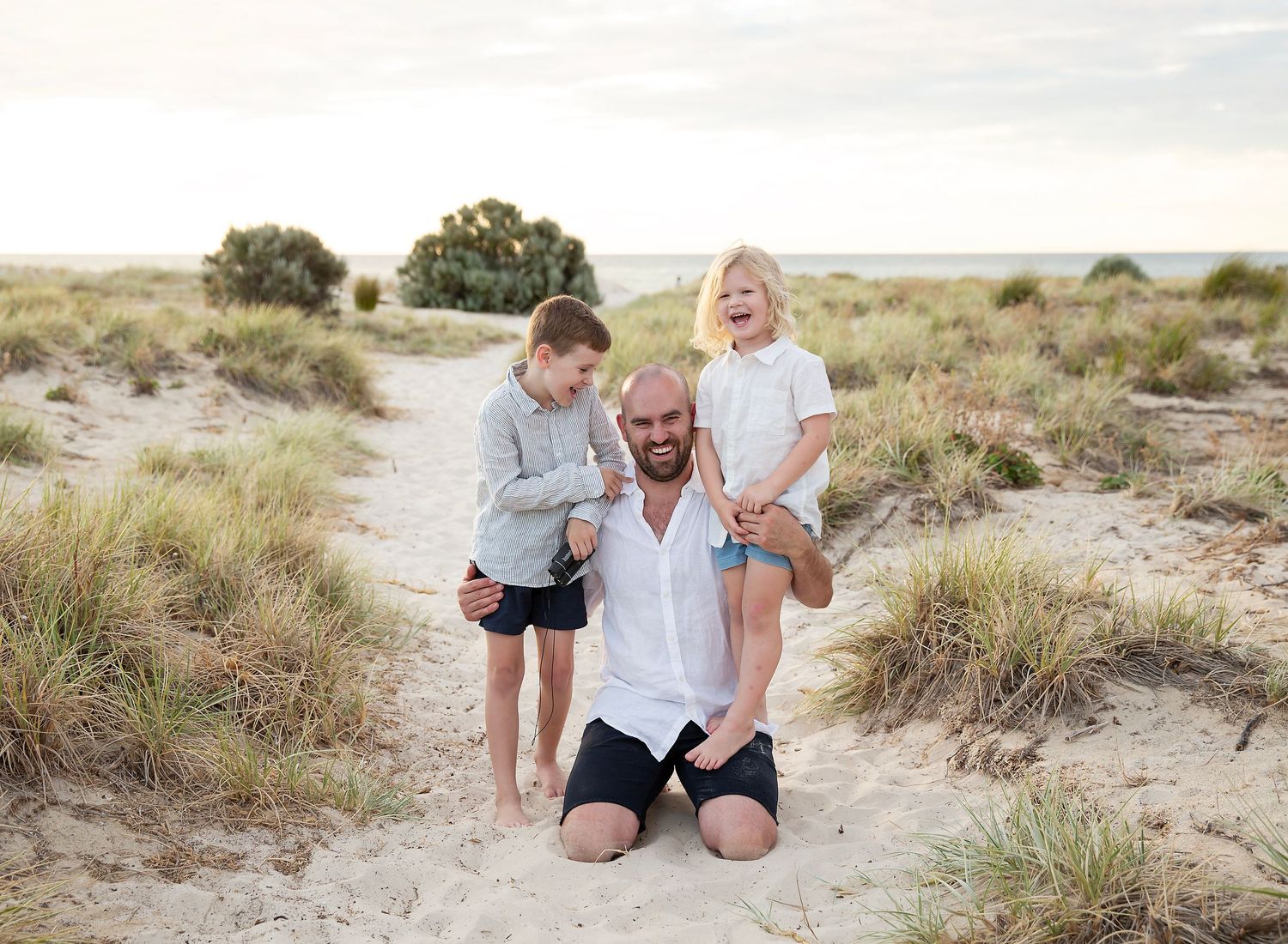 Dad and his two boys smiling in family photograph on the sand at golden hour in Largs Bay SA