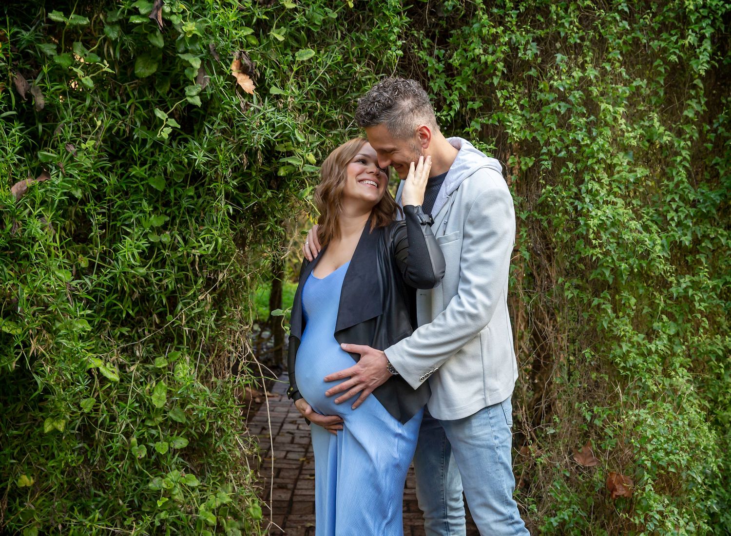 A couple lovingly staring and smiling at each other and cuddling their pregnancy bump in Maternity photoshoot in Adelaide Botanic Gardens.
