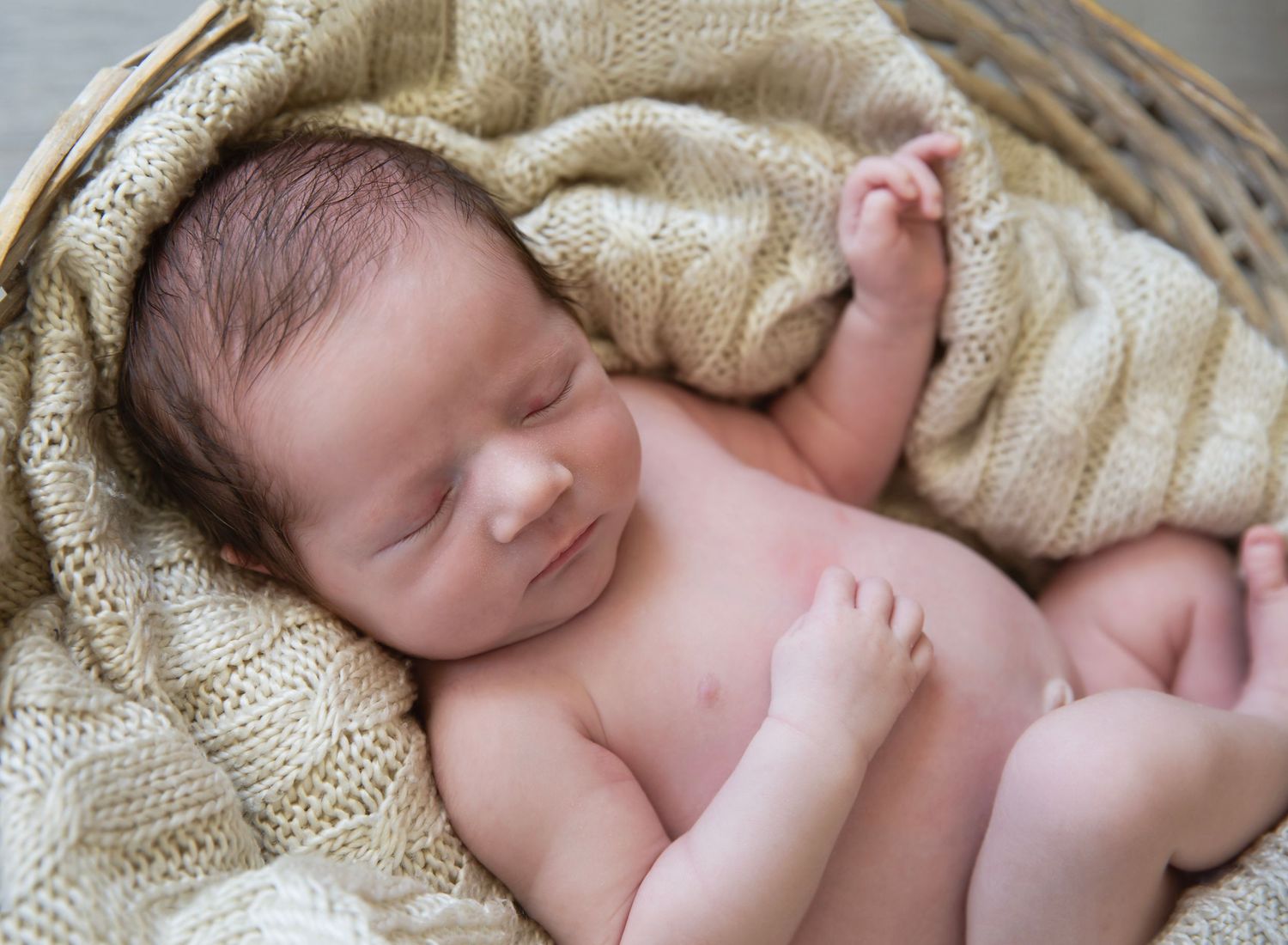 newborn baby posed in basket with neutral tone blankets