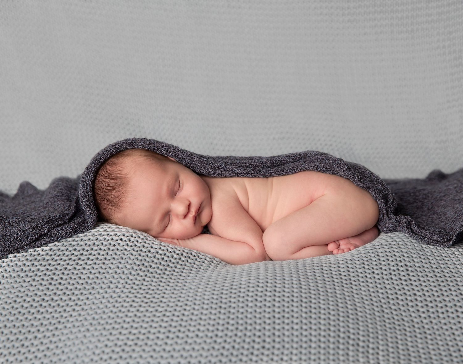 baby born posed on his tummy with hands and feet tucked and wrap draped over