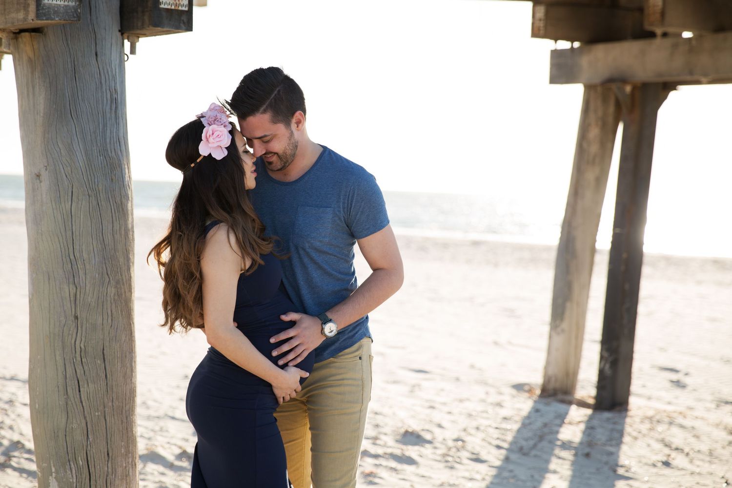 man looks lovingly at pregnant wife with her baby bump showing in sunset beach maternity session