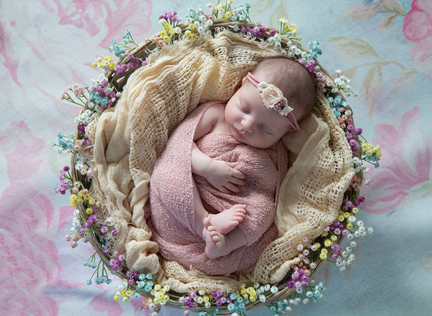 newborn girl in round basket with little flowers on it