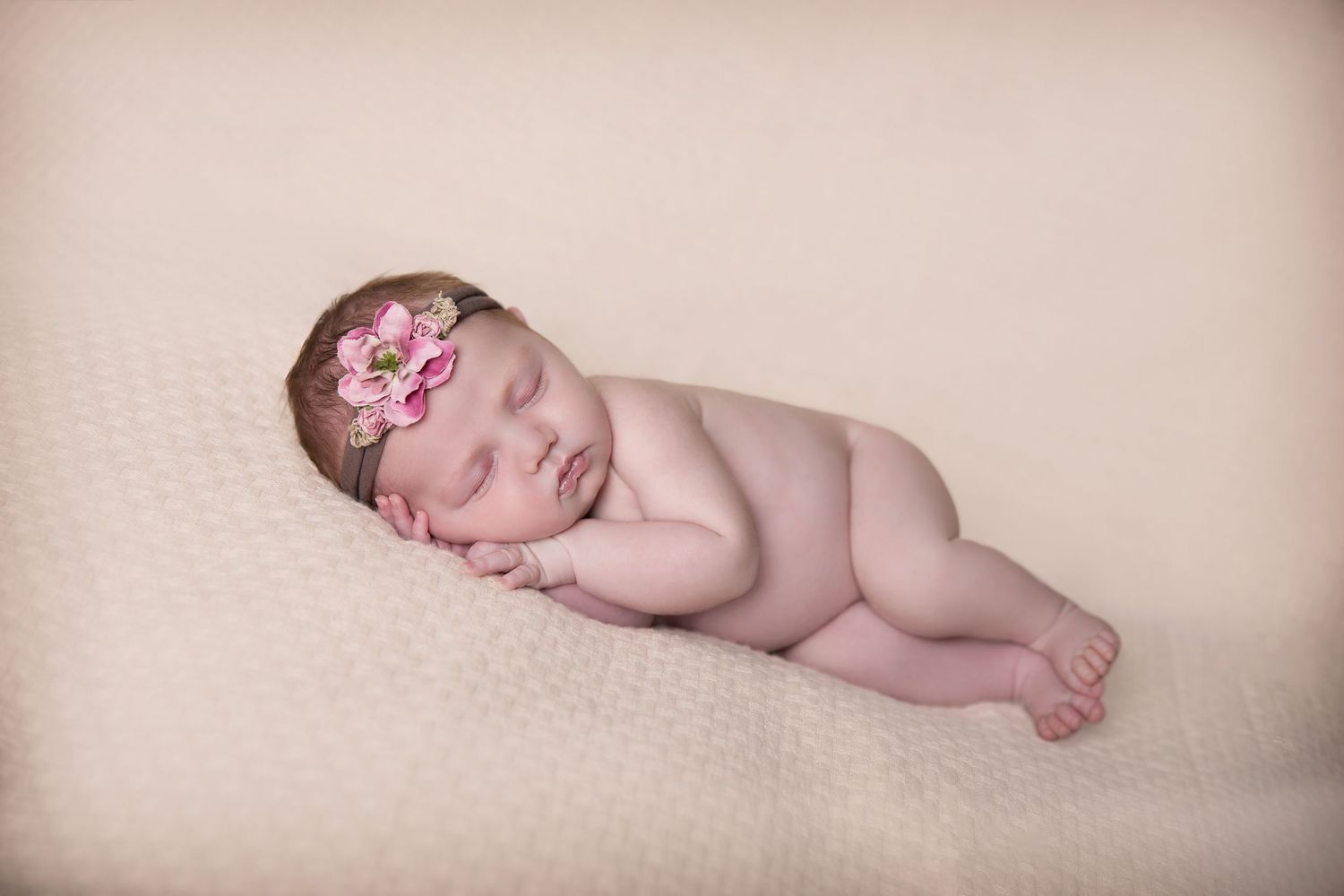 baby girl lying posed on peach knit blanket wearing flower crown settled with little fingers showing