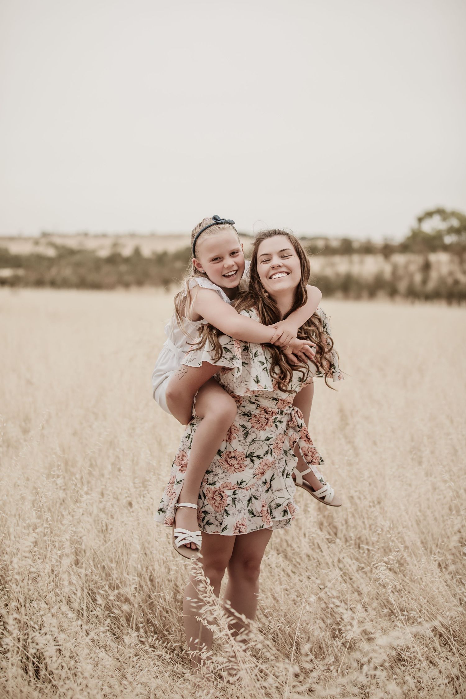 Chloe White the photographer smiling as she gives her daughter a piggy back in a field.