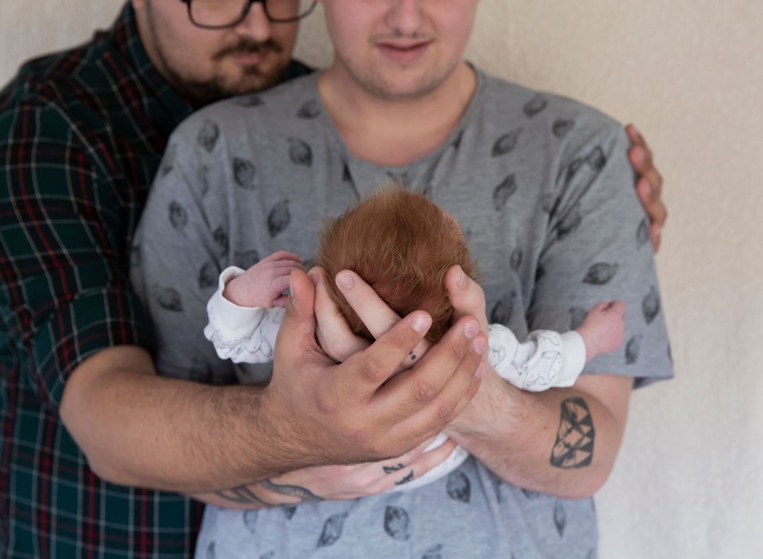 Two dads stare lovingly at the newborn baby cradled in their hands. In-home newborn photoshoot in Adelaide SA.