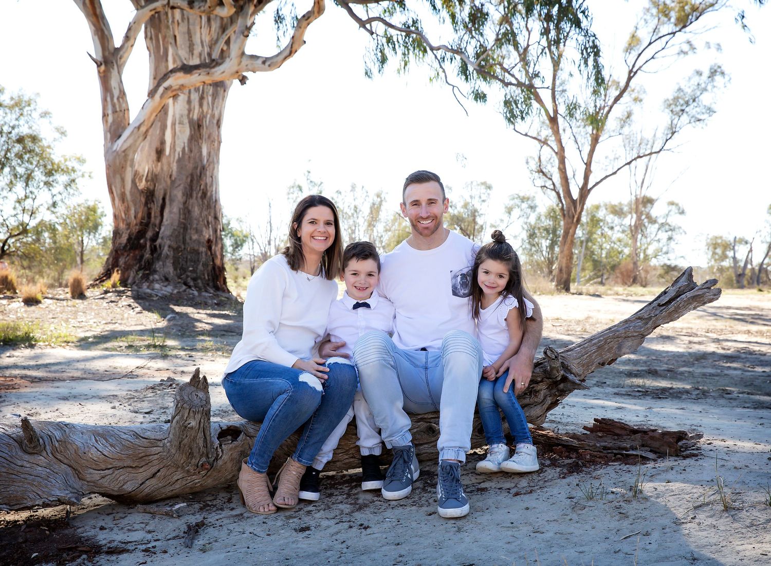 Family sitting cuddled together smiling on an old tree on the rivers edge in family photoshoot in Waikerie SA.