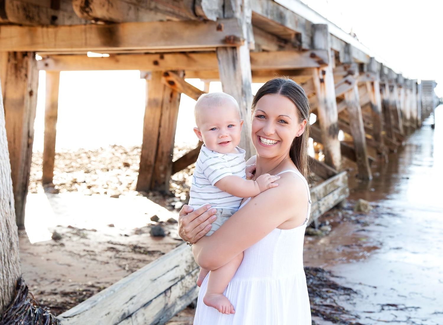 A mum smiling happing with her 6 month old baby in backlit photo at the Ardrossan Jetty.