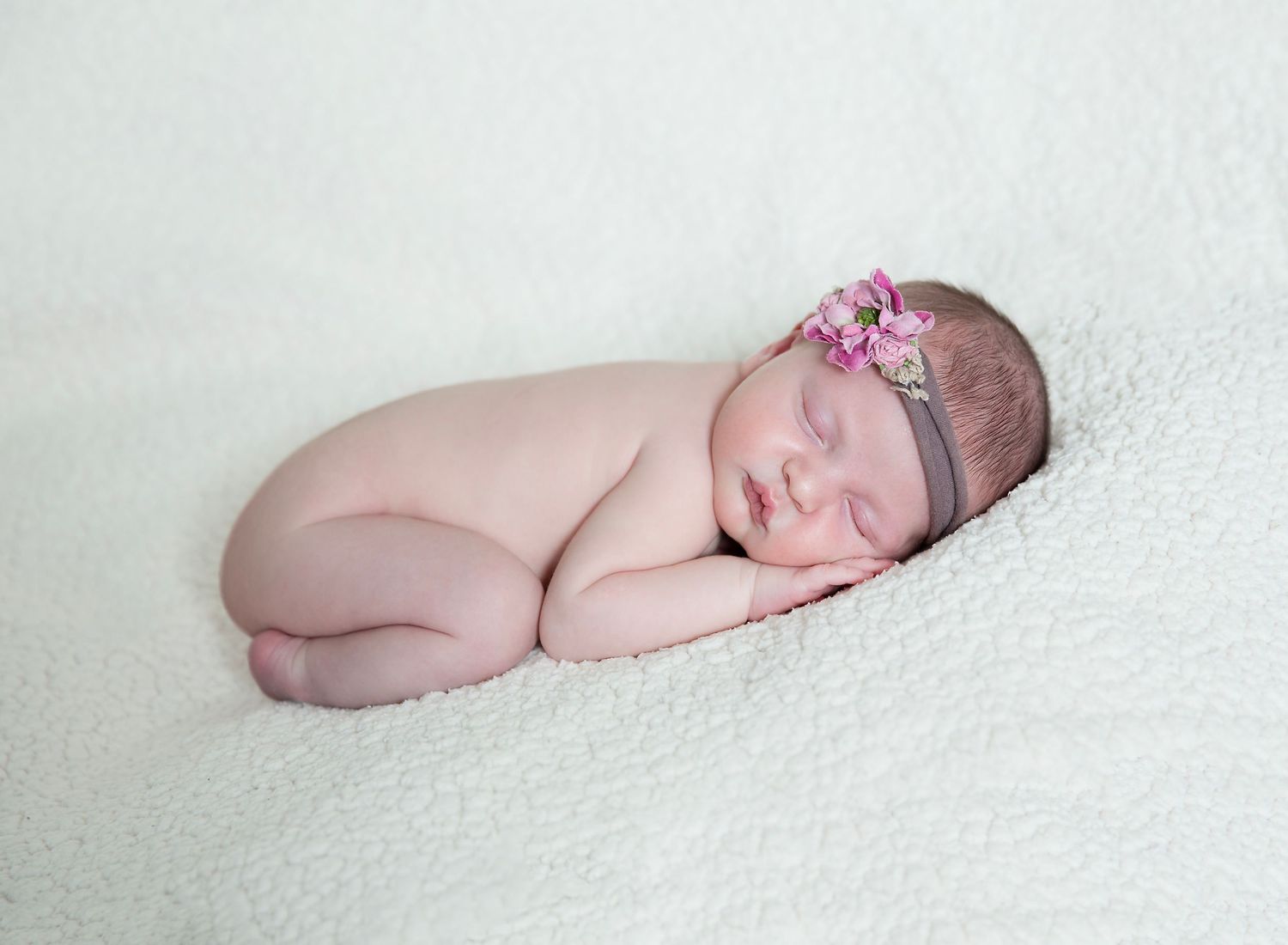 Baby girl in floral headband posed on cream backdrop for studio photo