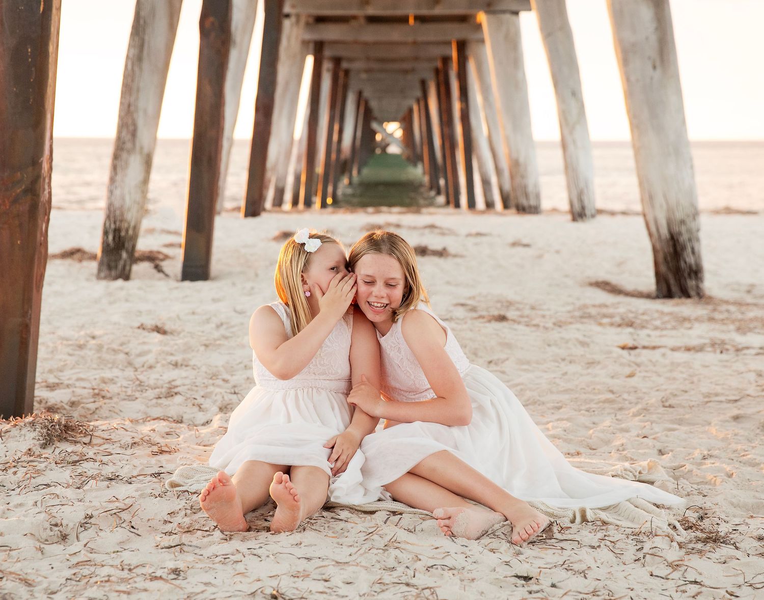 two sisters whispering a secret to each other under the Largs Bay jetty for family photography at sunset