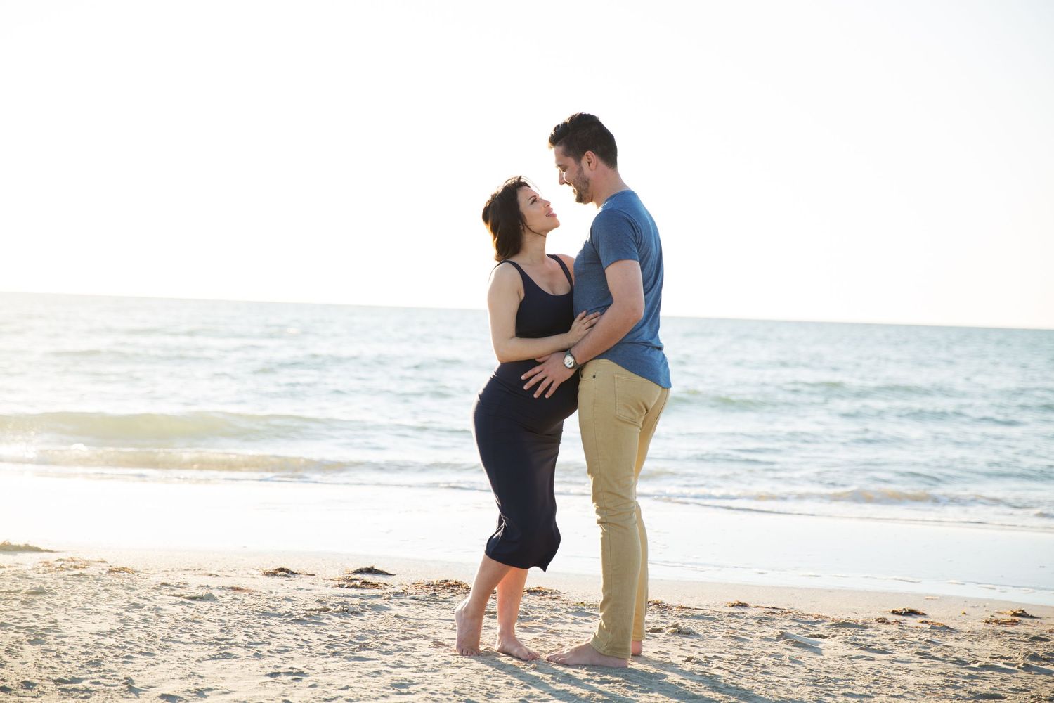 Wife lovingly cuddling husband at Largs Bay beach SA in pregnancy maternity photography session.