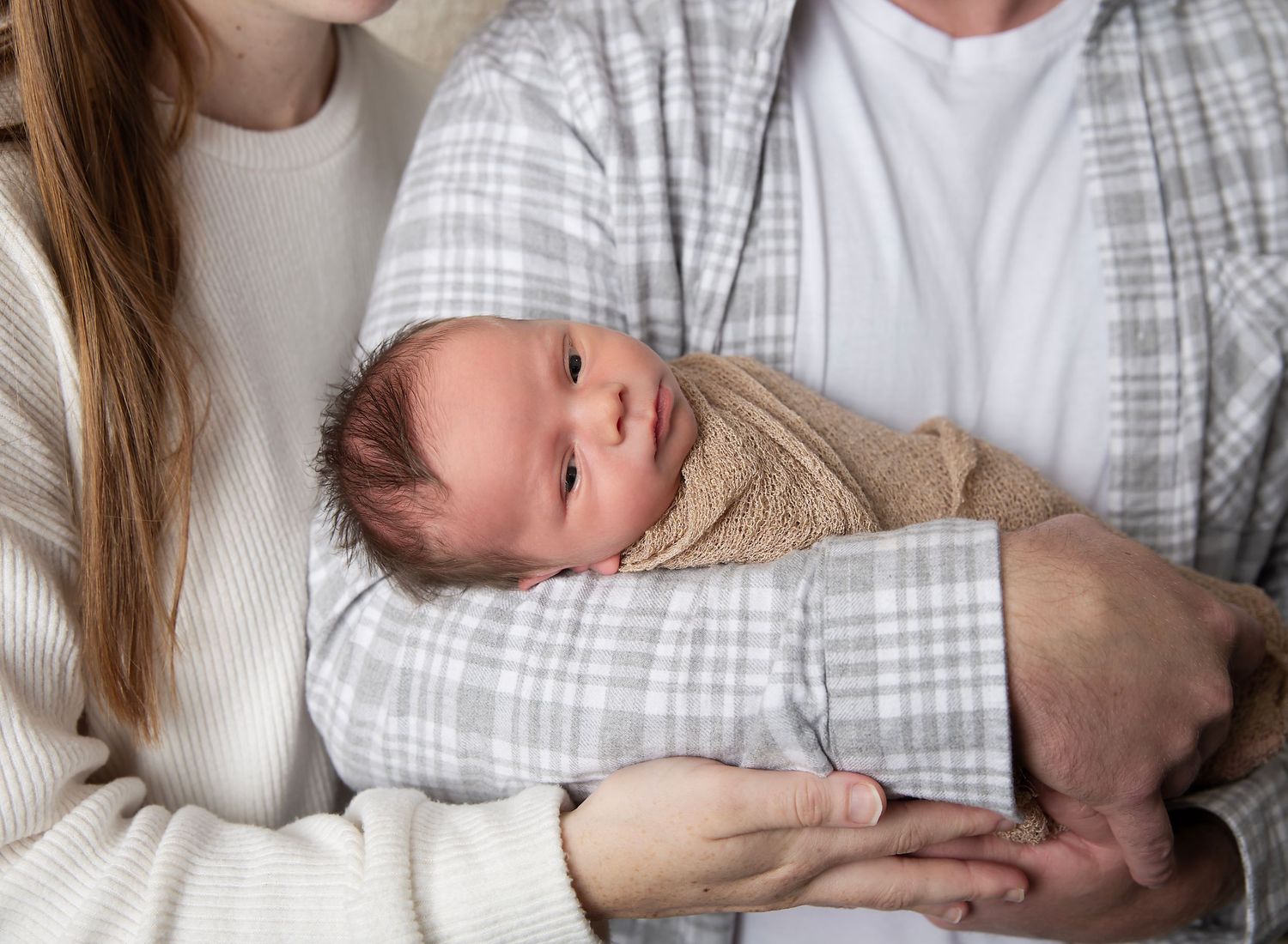 First-time parents holding their newborn and smiling during in-home session