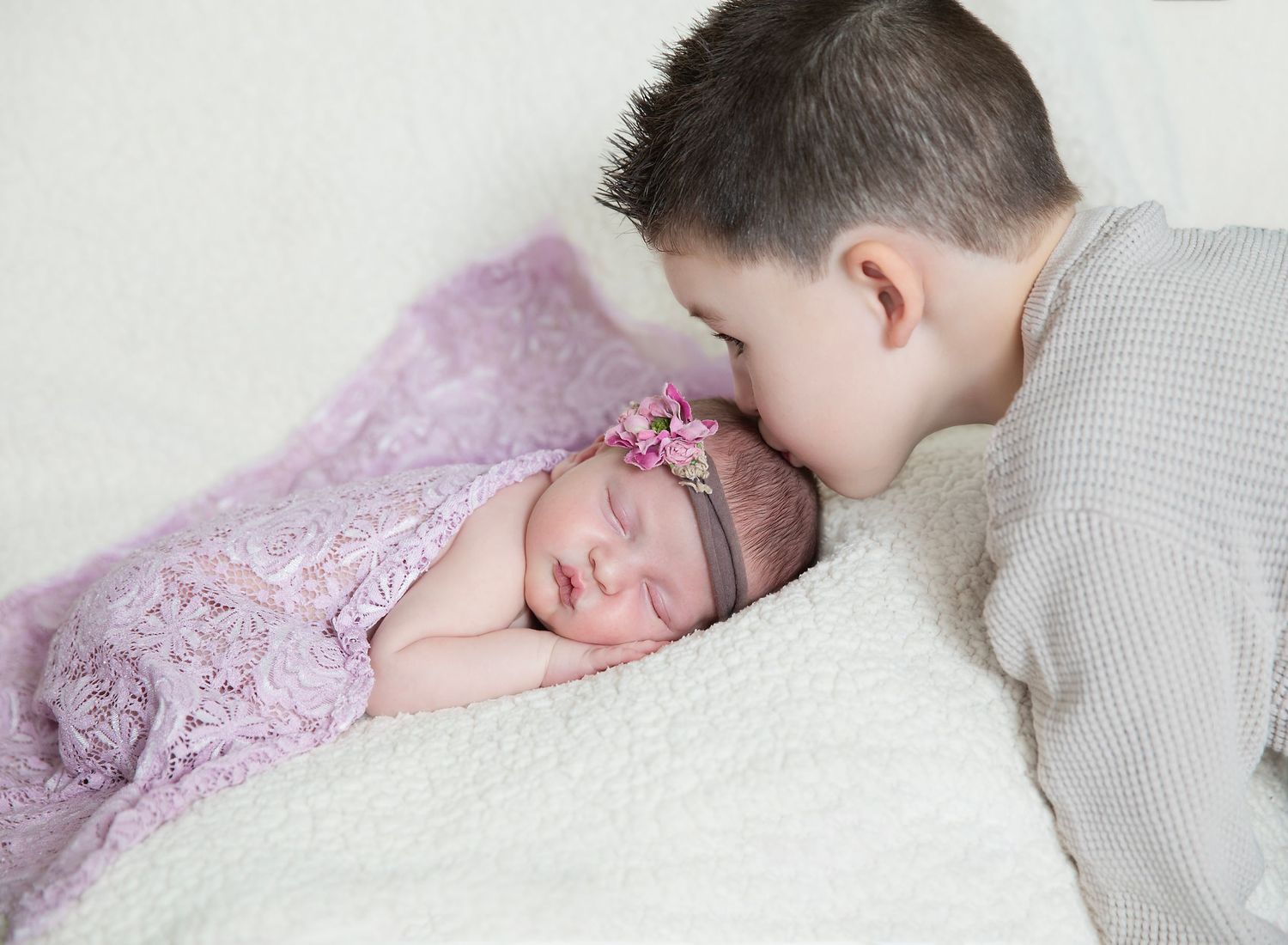 Big brother gently kissing newborn sibling on forehead