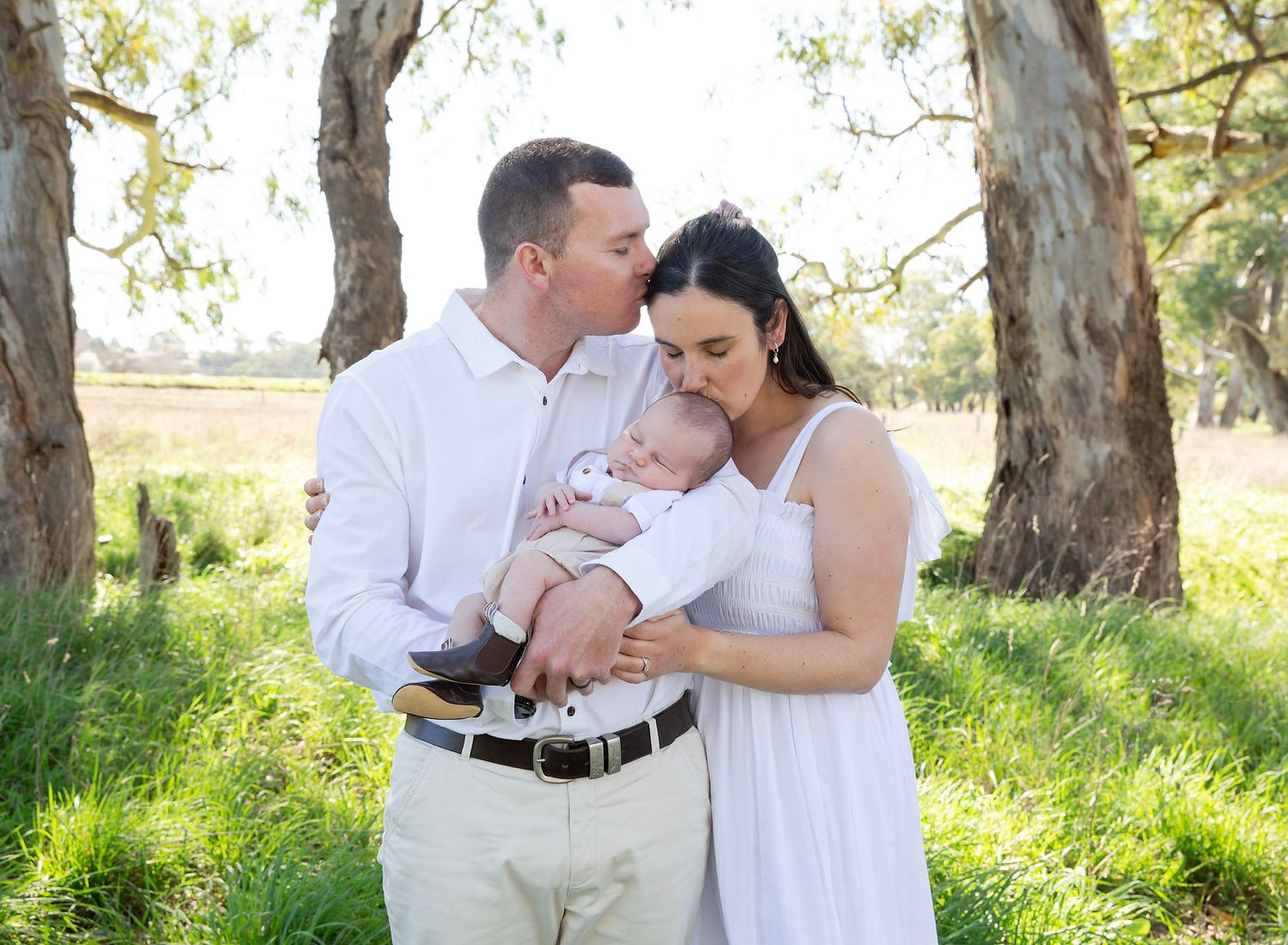 Two new parents embracing each other over their peacefully sleeping newborn baby in outdoor newborn session in Mt Barker SA