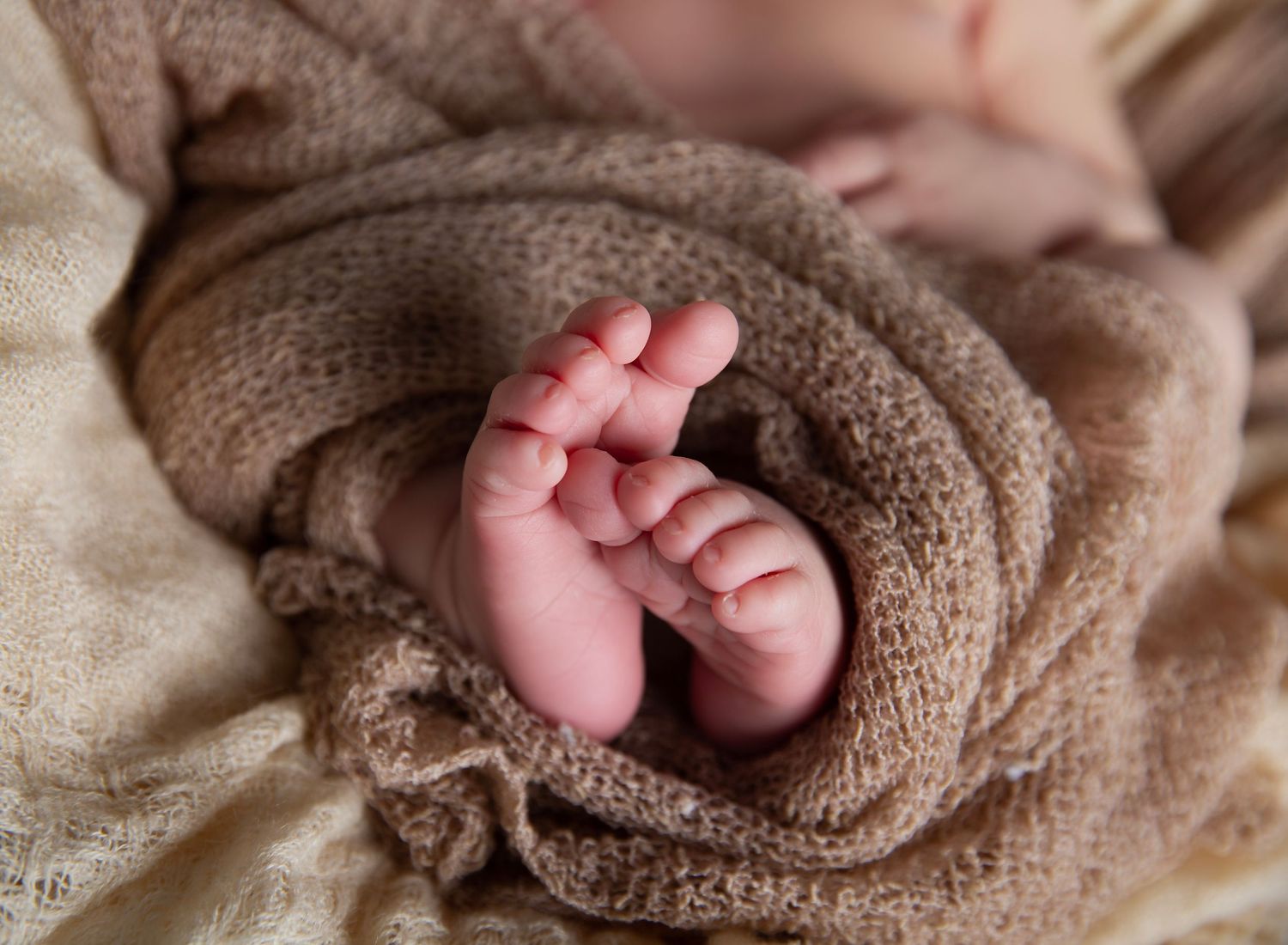 Close-up of tiny newborn feet wrapped in a soft beige swaddle