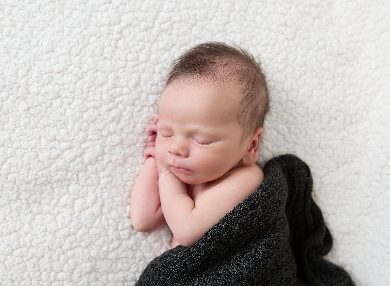 close up shot of sleeping newborn with his hands tucked under his head