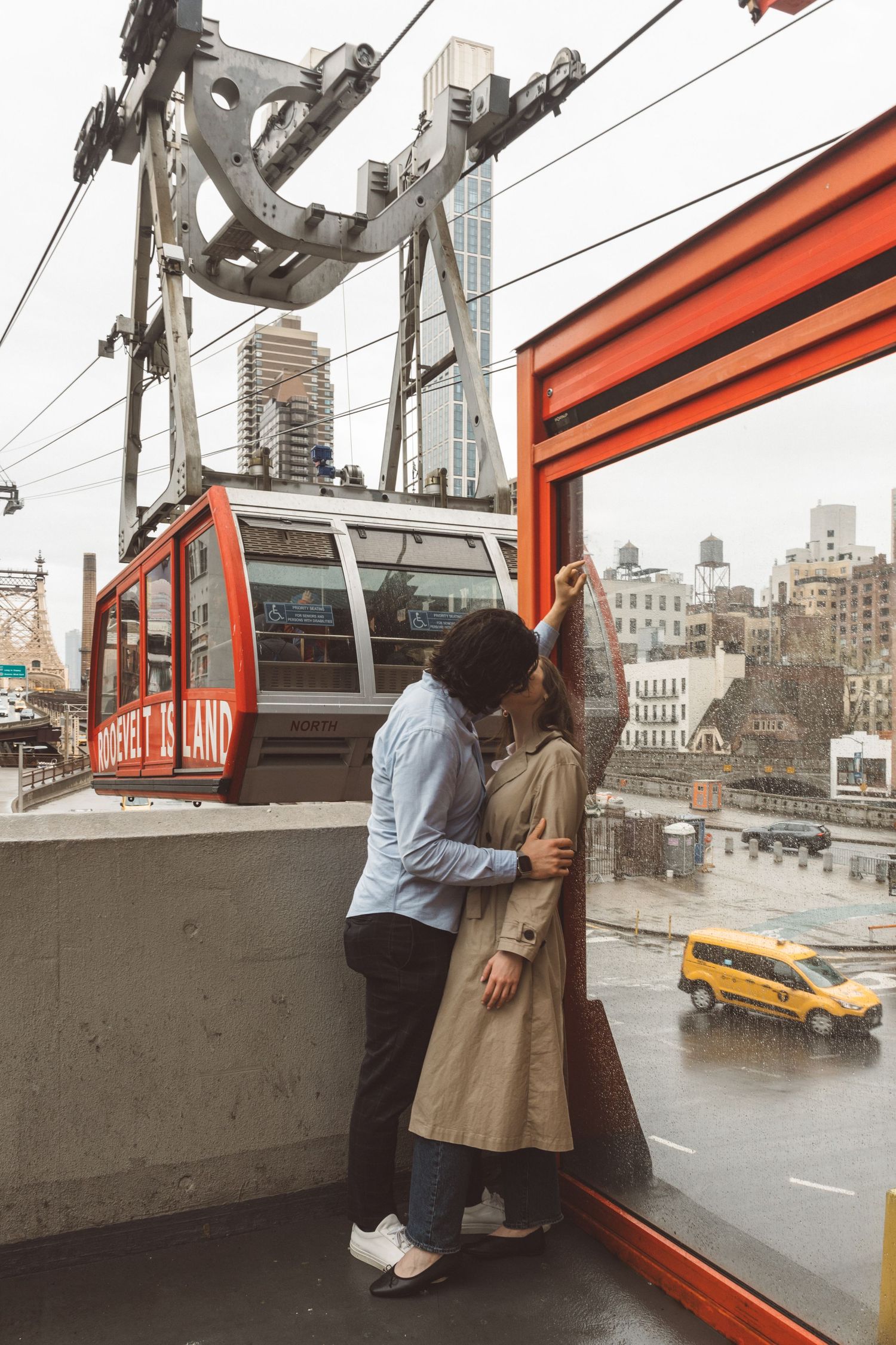 Editorial-style photo of couple sharing a kiss on a rainy day by the Roosevelt Island tram