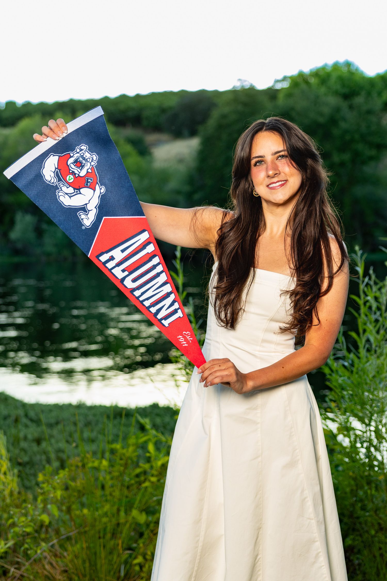 Fresno state graduate with university banner wearing a white dress at Lost Lake in Fresno California