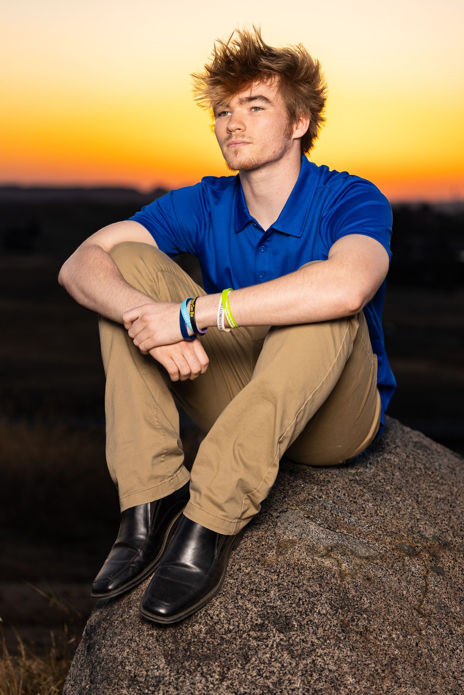 High school senior wearing a blue polo with khaki pants sitting in a boulder during sunset in Fresno California.