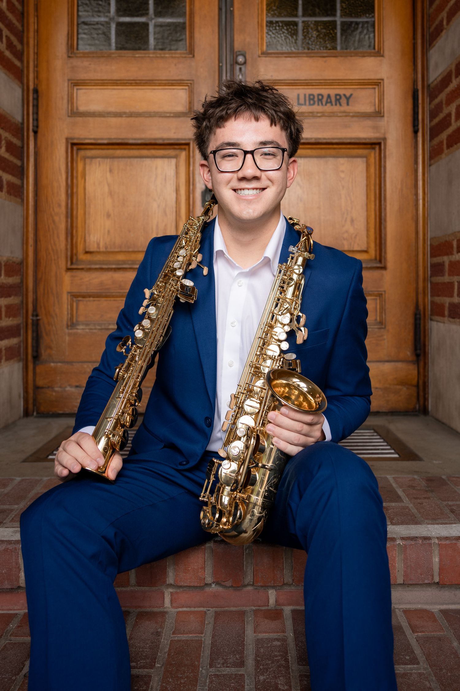 Clovis North High School senior wearing a blue suit with two saxophones at the library of Fresno City College.