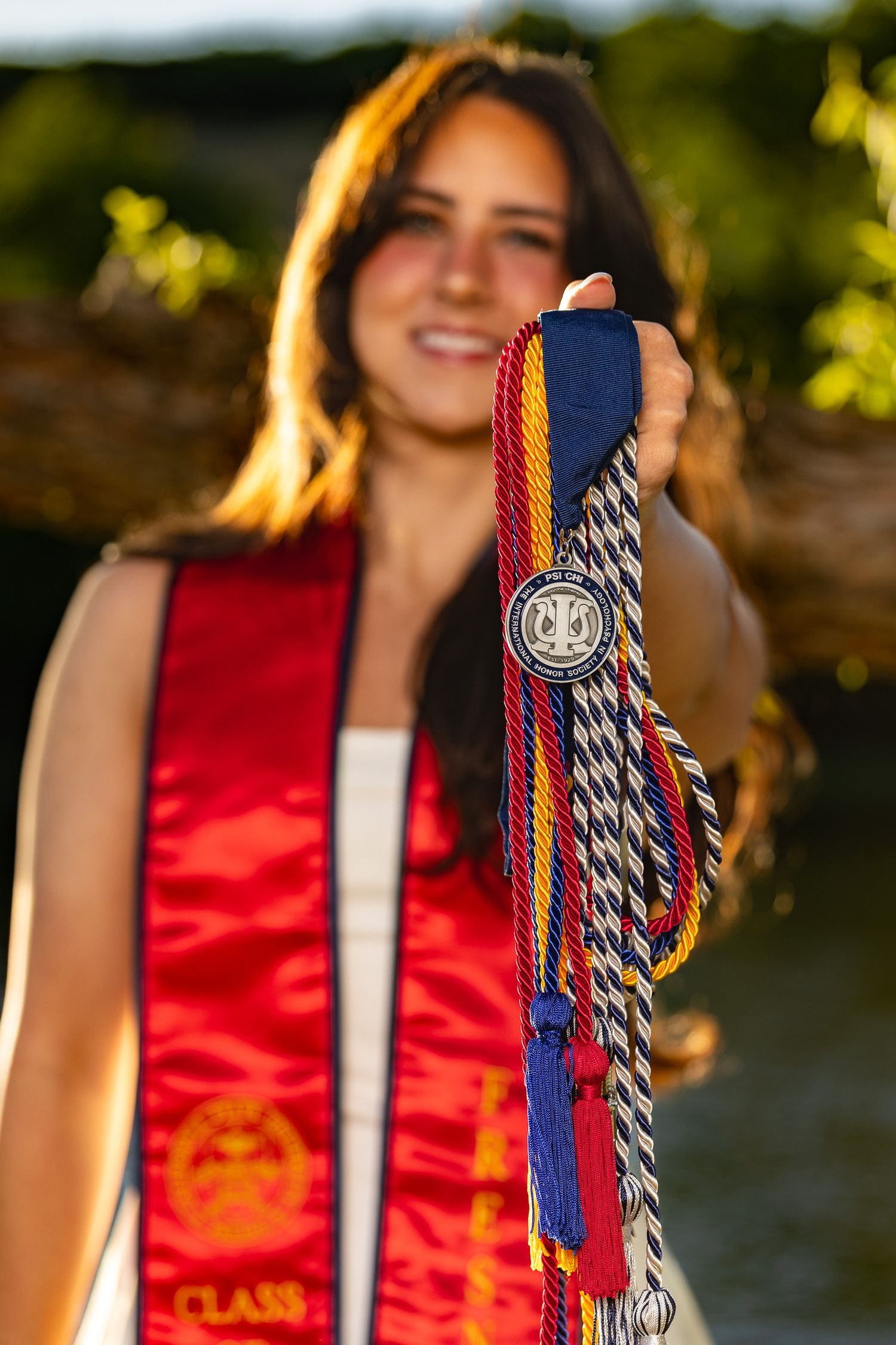 Fresno state graduate posing with medals, ribbons and stole wearing a white dress at Lost Lake in Fresno California