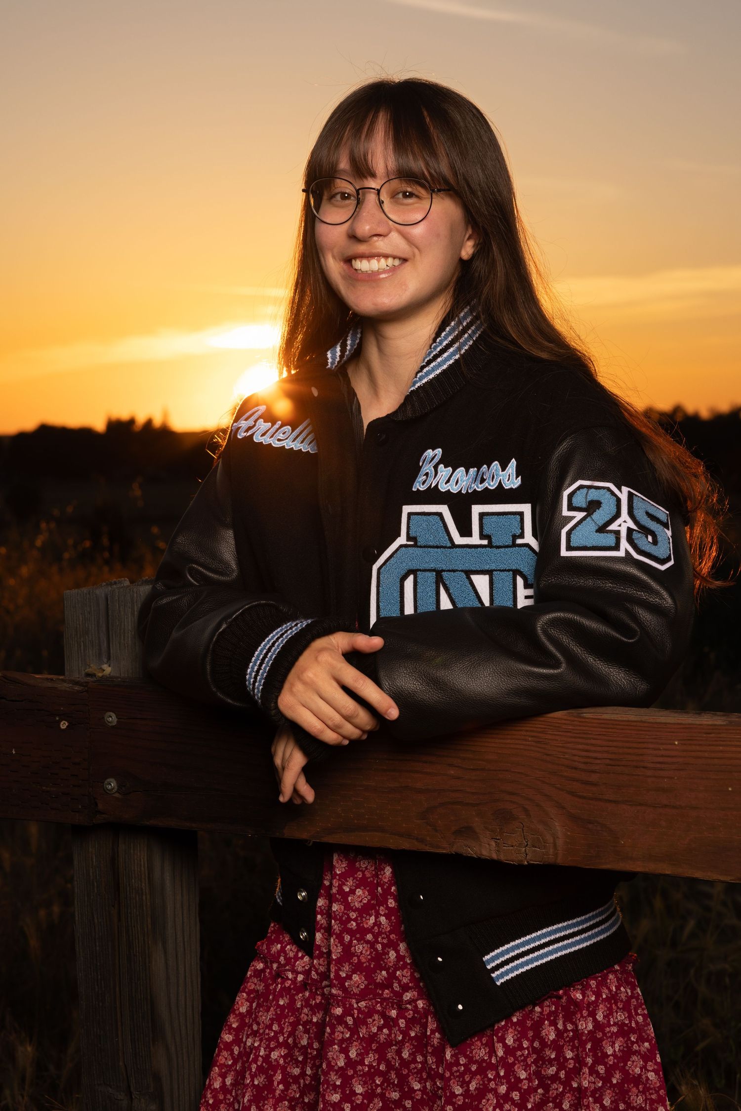 Clovis North High School senior wearing a letterman jacket at Woodward park during sunset.