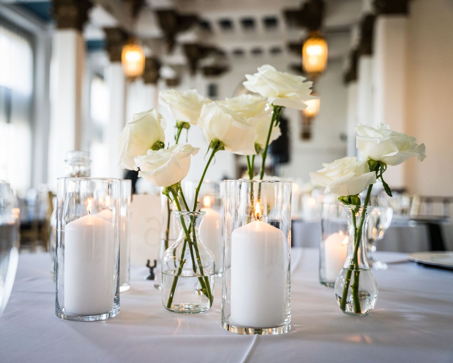Elegant wedding reception table with white floral centerpieces and glowing candles.