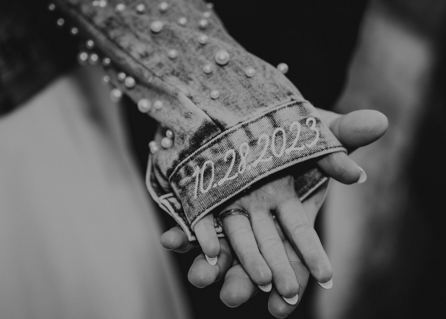 Black and white close-up of hands wearing ornate jewelry in intimate moment.