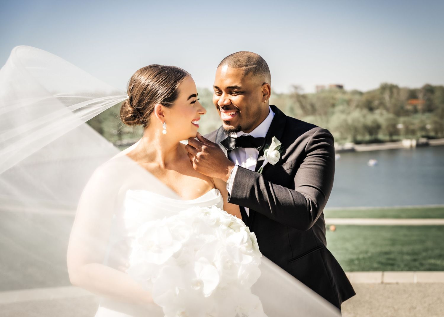 A romantic wedding moment captured by the water with flowing veil and formal attire.