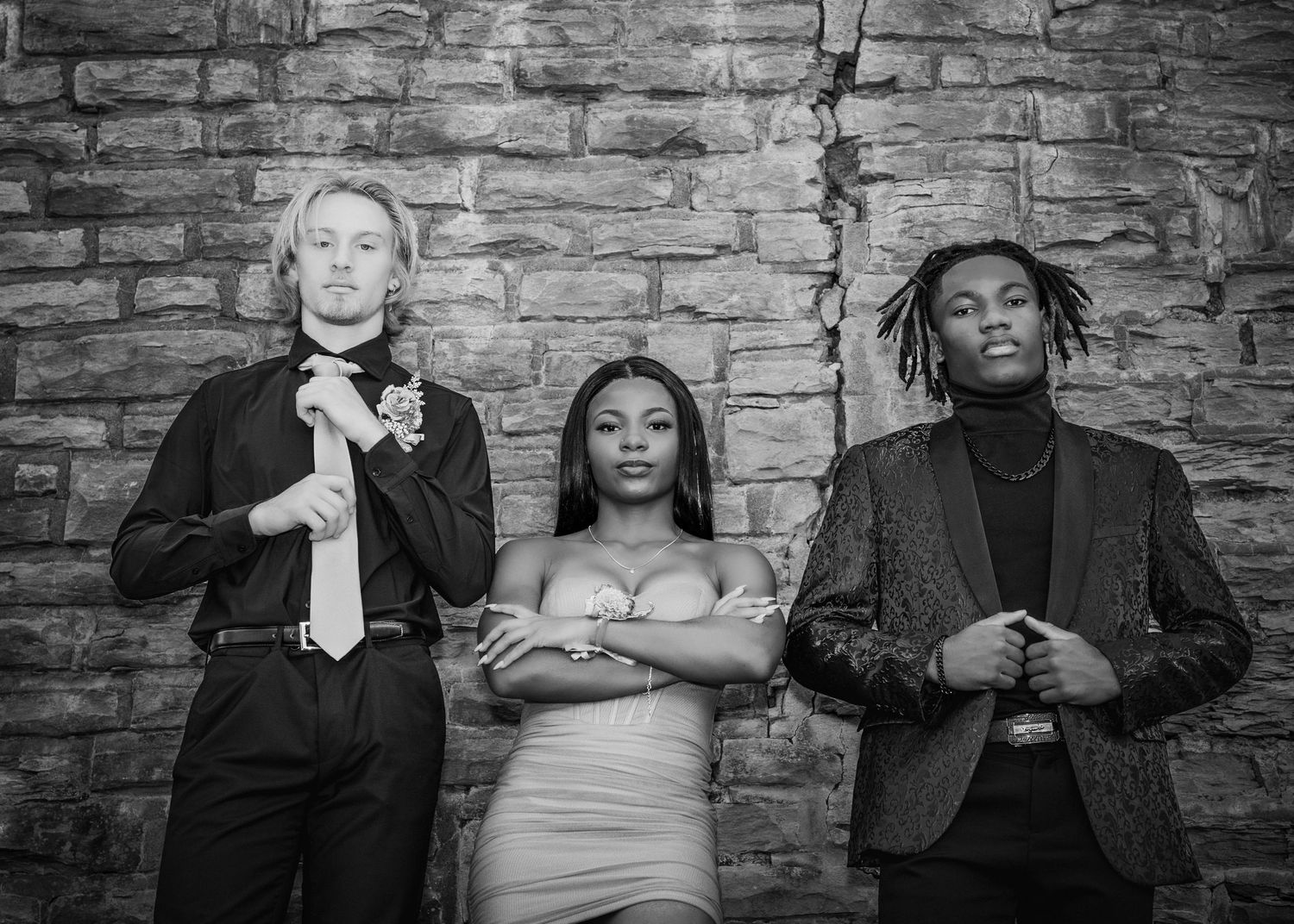 Three stylish people pose against a rustic brick wall in black and white photography.