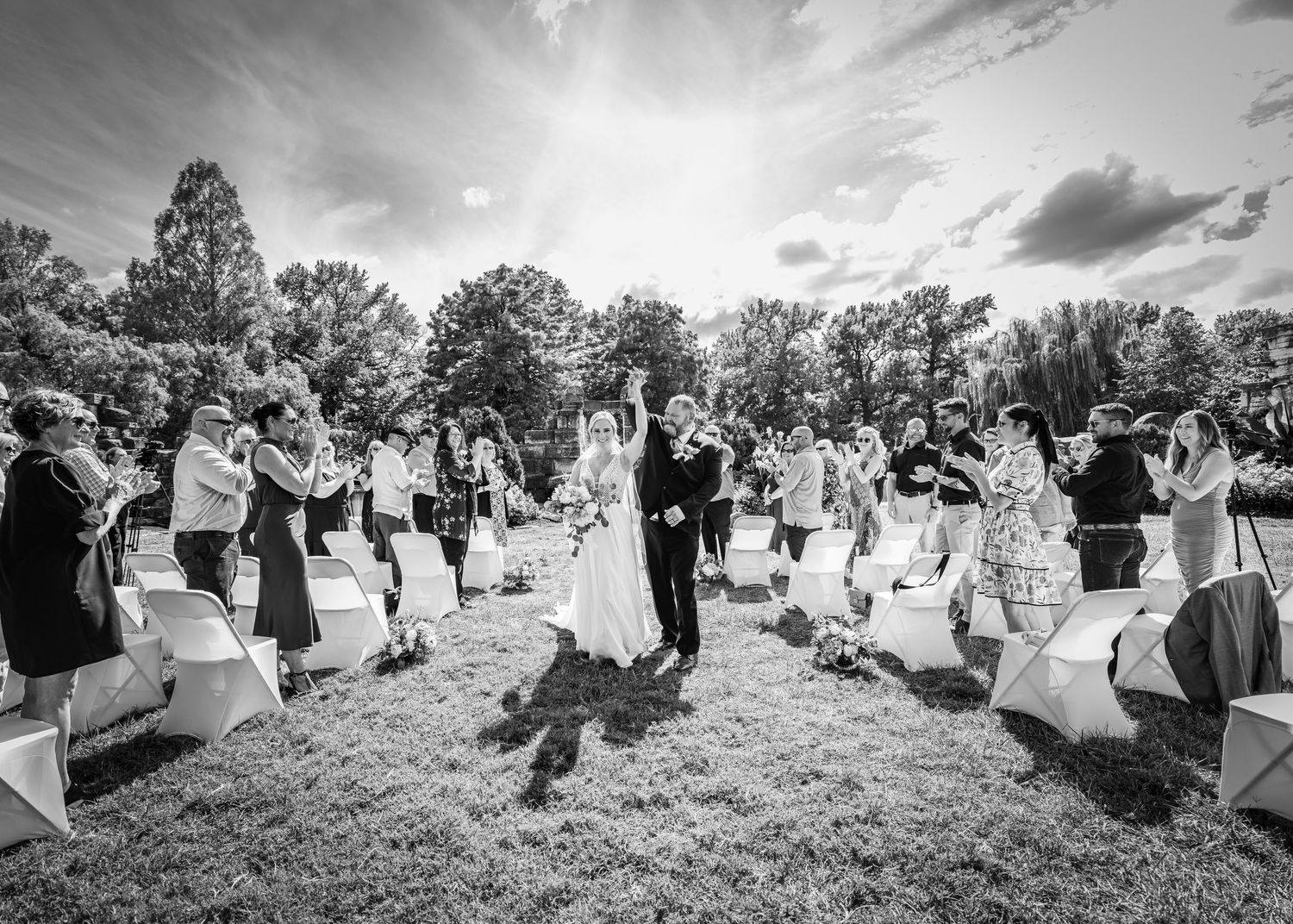 Black and white image of a wedding celebration in a garden with guests standing along a pathway.