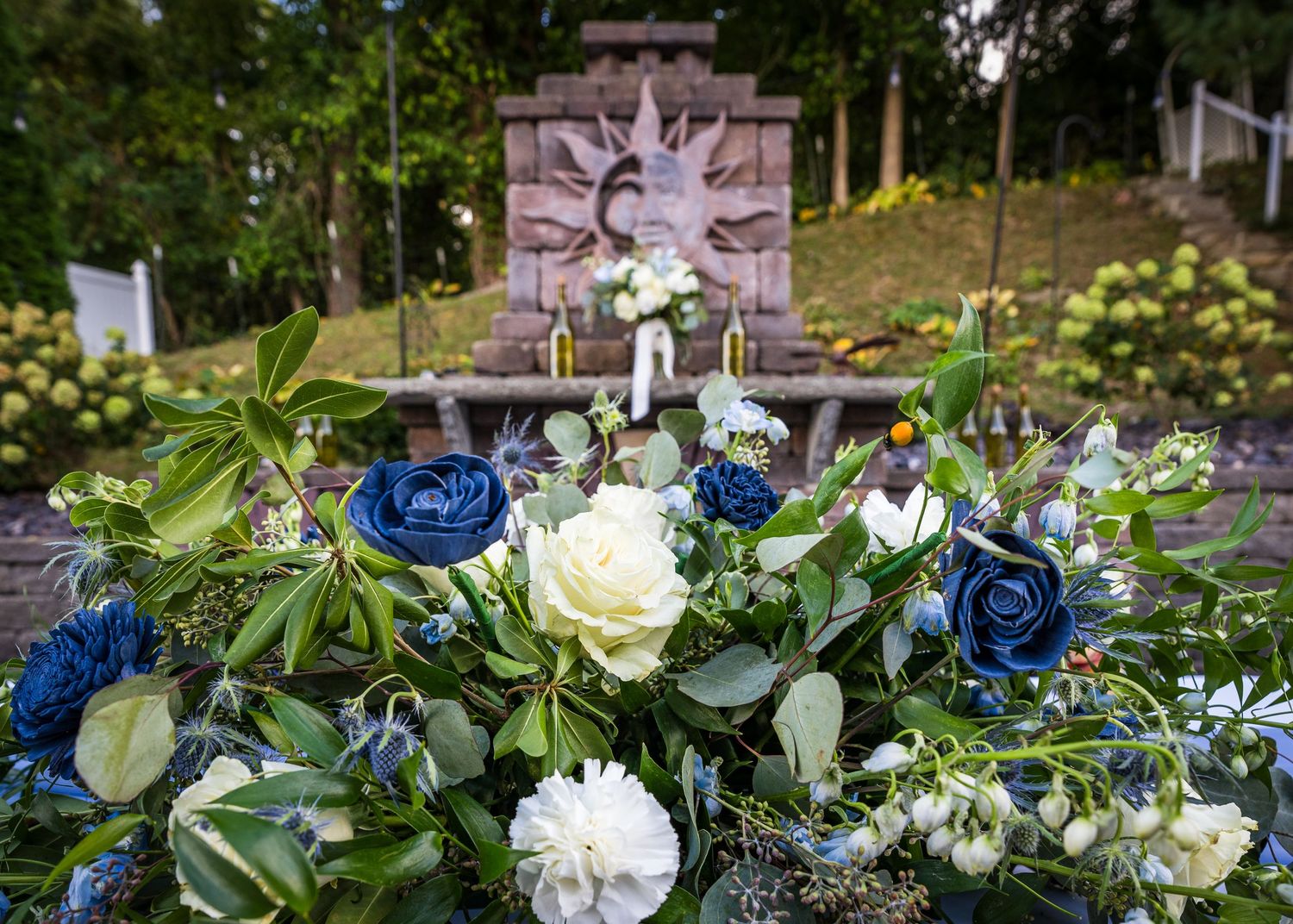 Elegant floral arrangement with blue roses and white flowers against an ornate backdrop in a garden setting.