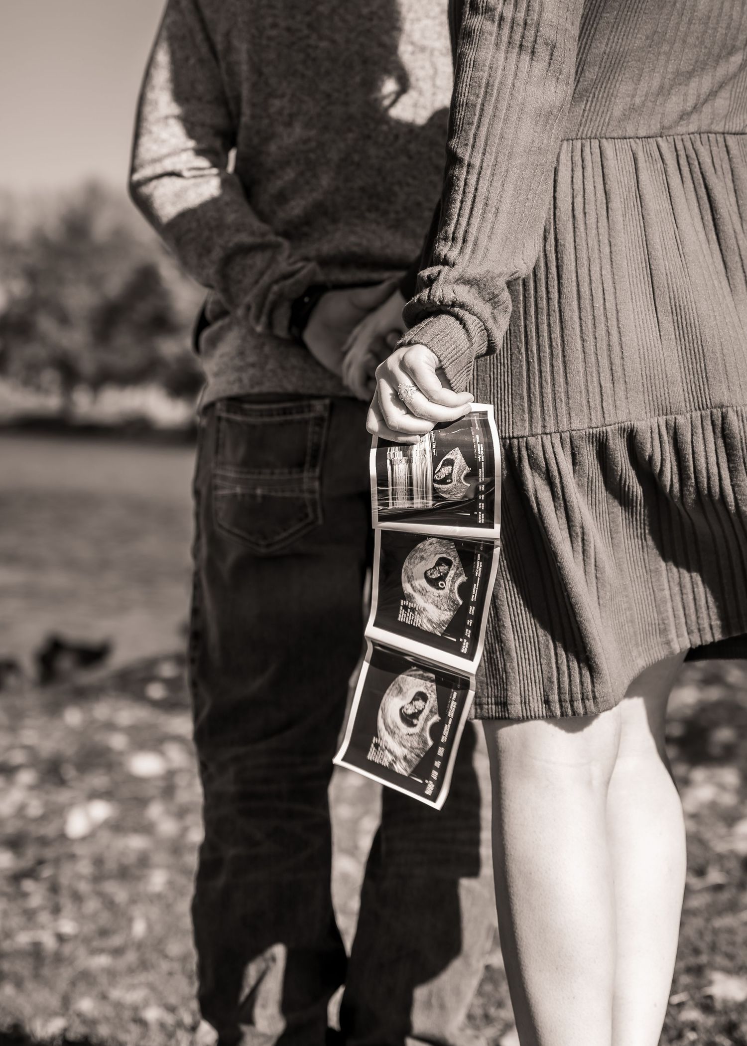 Black and white photo of couple holding ultrasound photos in an outdoor pregnancy announcement.