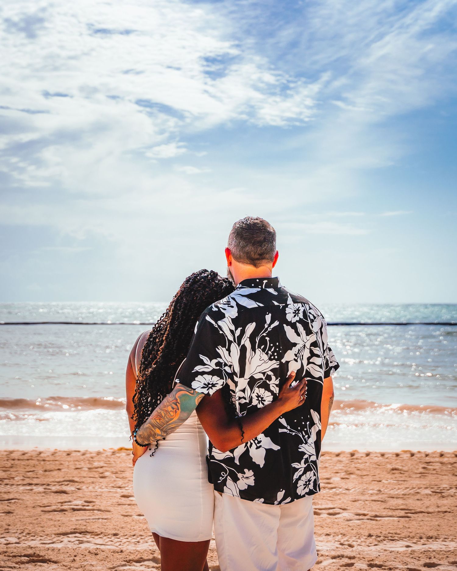 Couple in matching floral shirts embracing on beach at sunset.