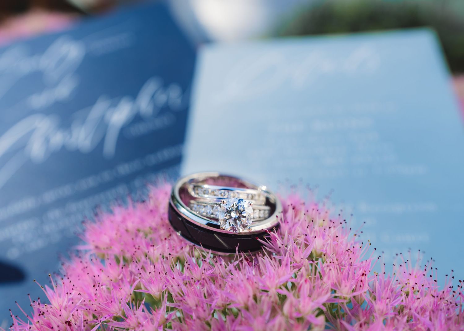 Wedding ring photographed on pink flowers against a blue background.