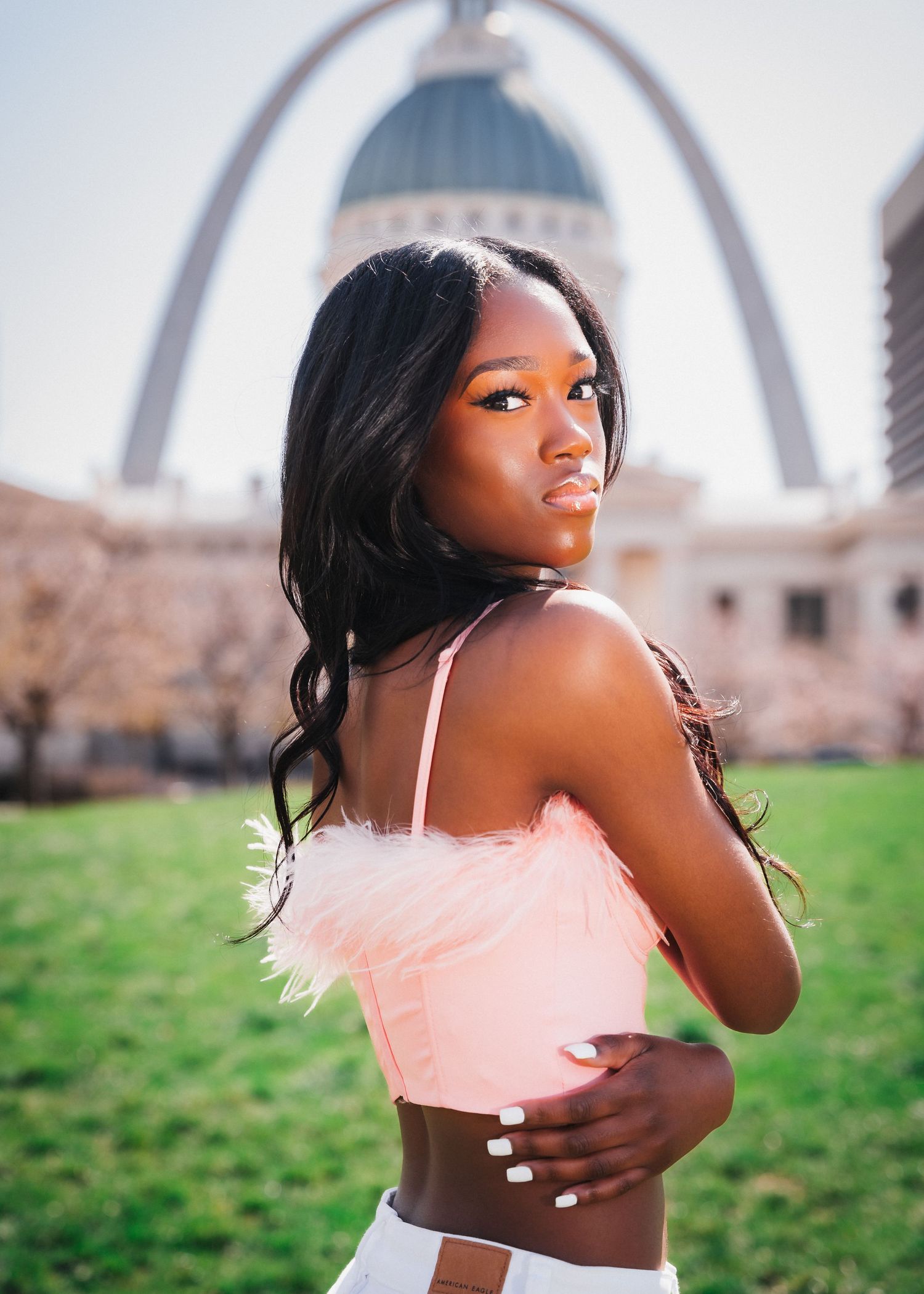 Elegant portrait in pink top with St. Louis Arch visible in background.